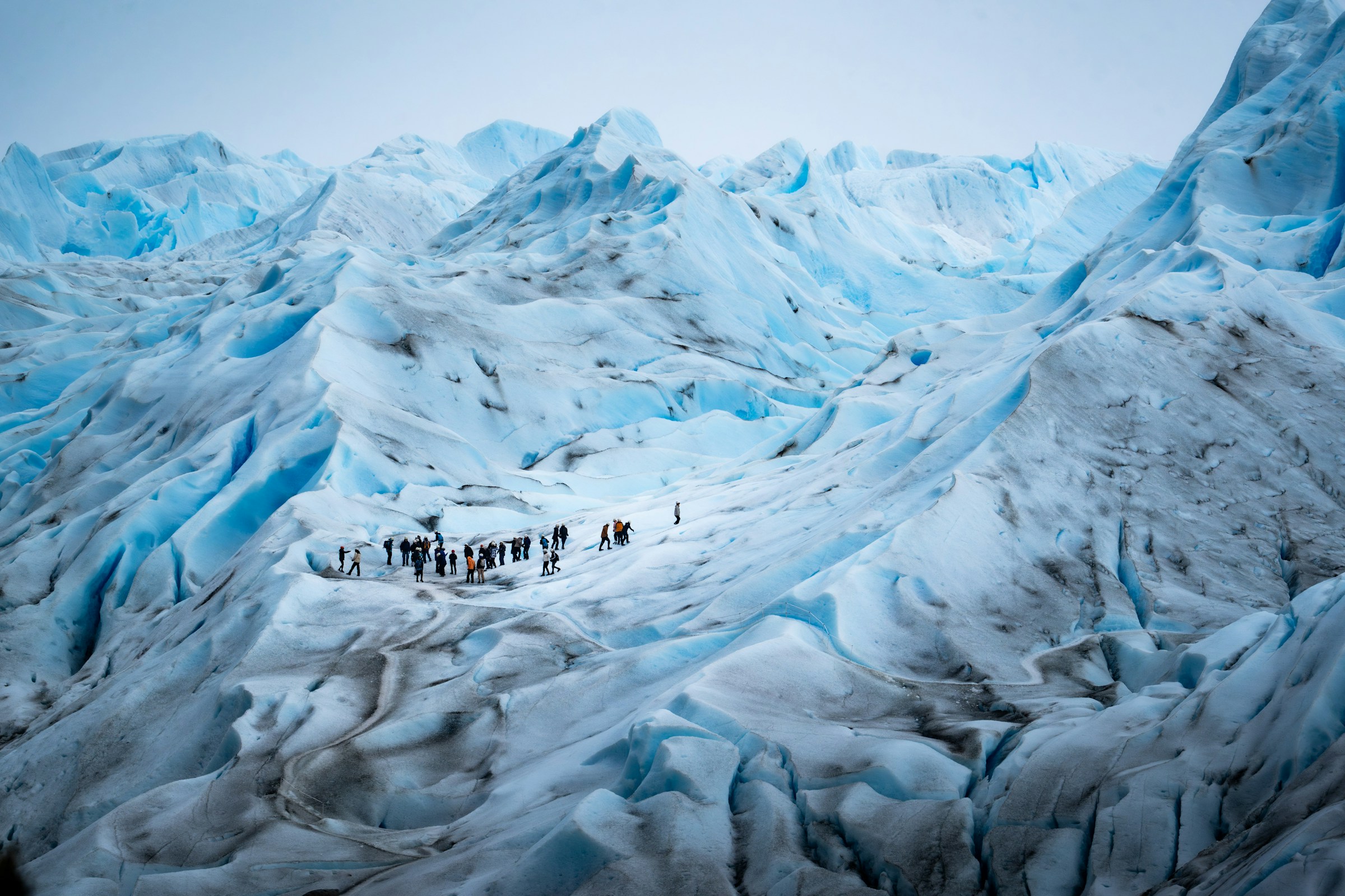 The vast blue face of Perito Moreno Glacier descends into a lake surrounded by Andean peaks.