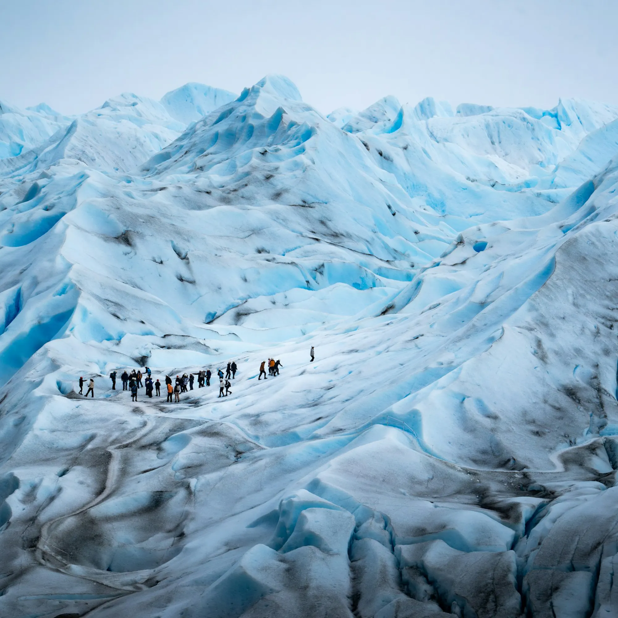The vast blue face of Perito Moreno Glacier descends into a lake surrounded by Andean peaks.