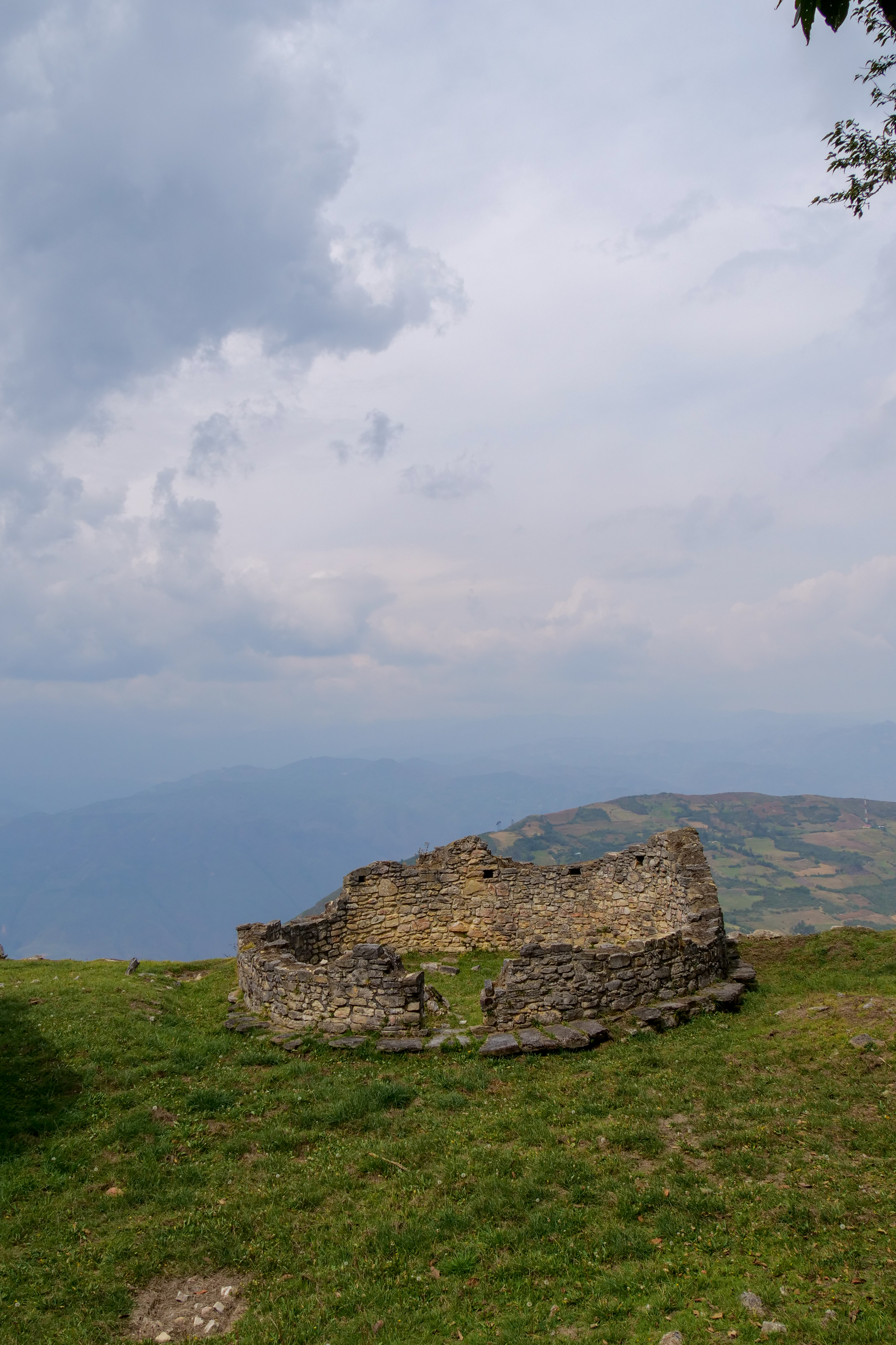 Ancient stone walls and circular dwellings of the Kuelap fortress rise among mist and greenery.