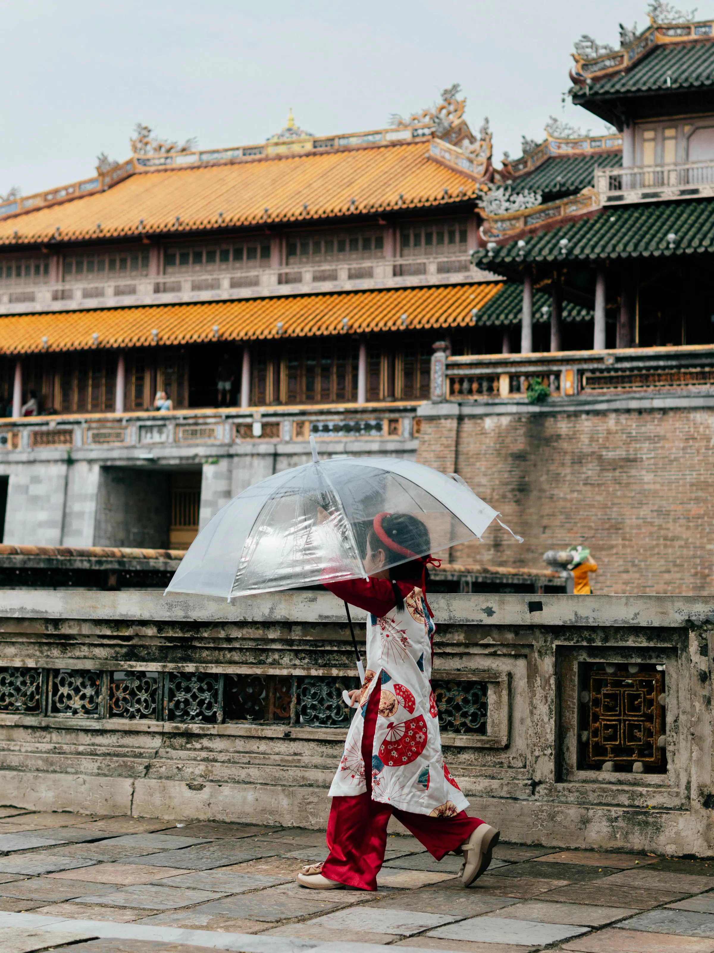 A woman in traditional ao dai walks past ornate yellow walls at the Imperial Citadel in Hue.