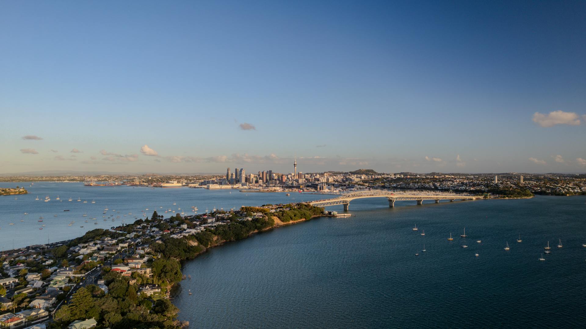 Aerial view of Auckland's harbour bridge and city skyline across the blue Waitemata Harbour.
