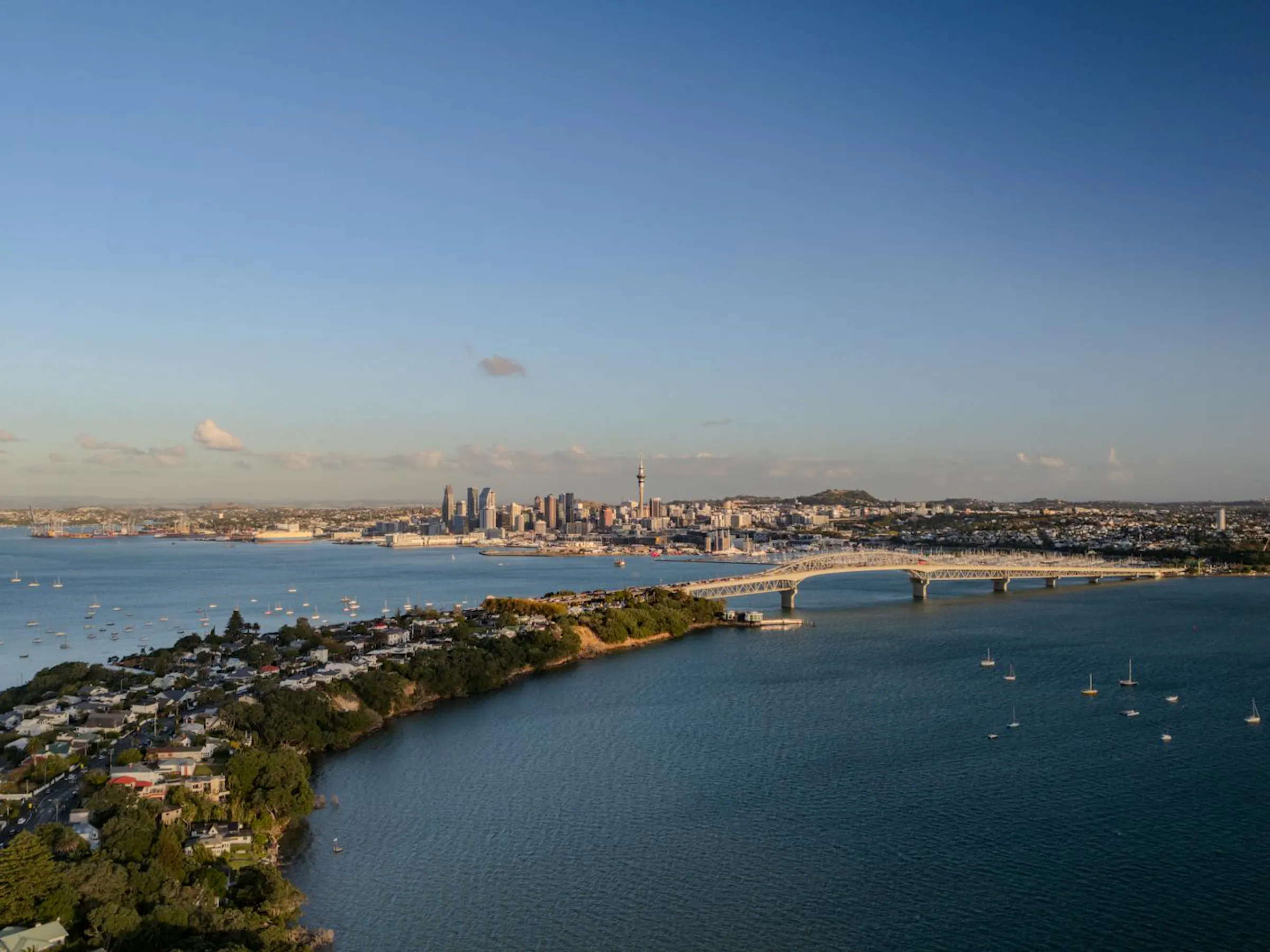Aerial view of Auckland's harbour bridge and city skyline across the blue Waitemata Harbour.