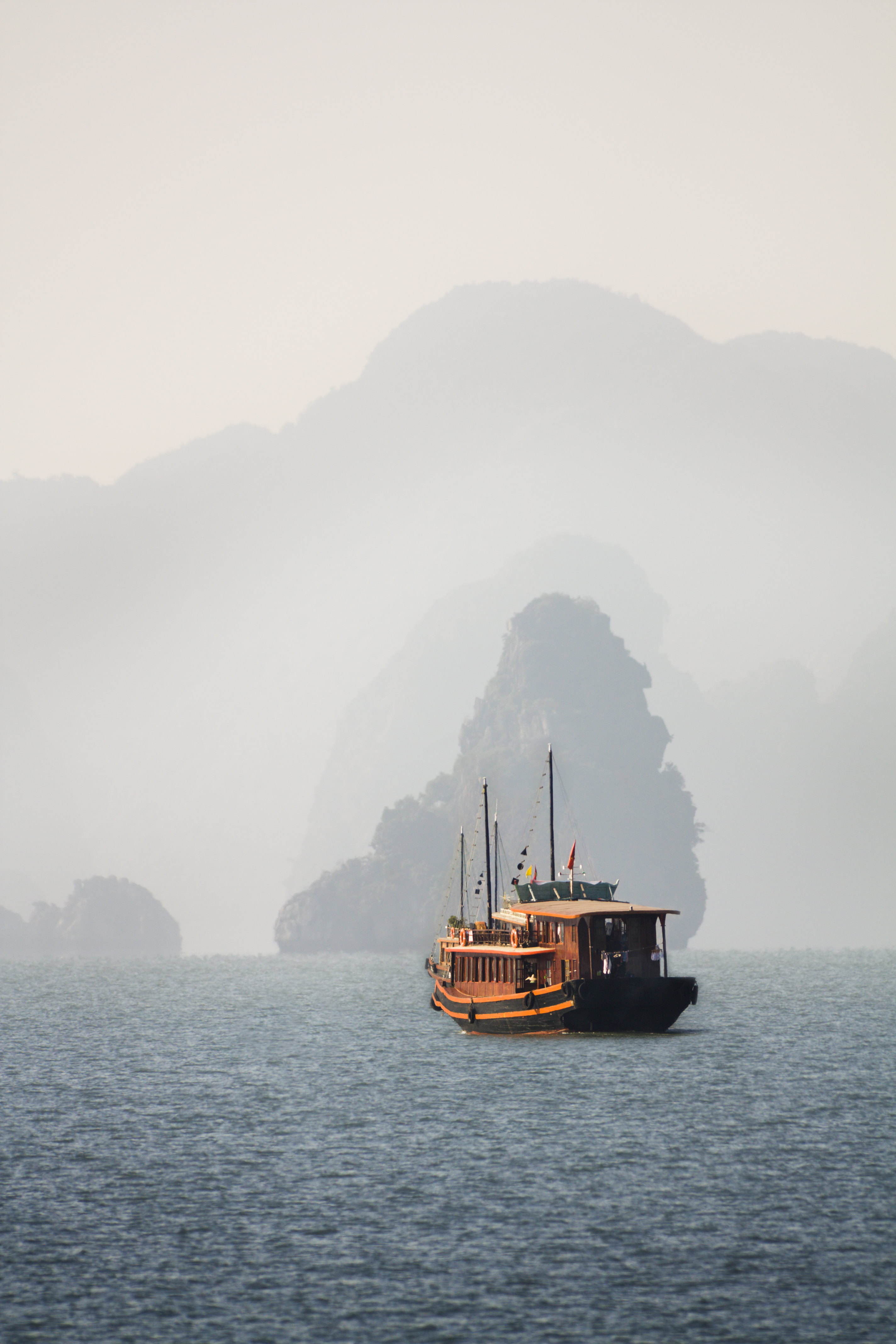 A large white cruise yacht anchors in still waters surrounded by limestone karsts in Ha Long Bay.