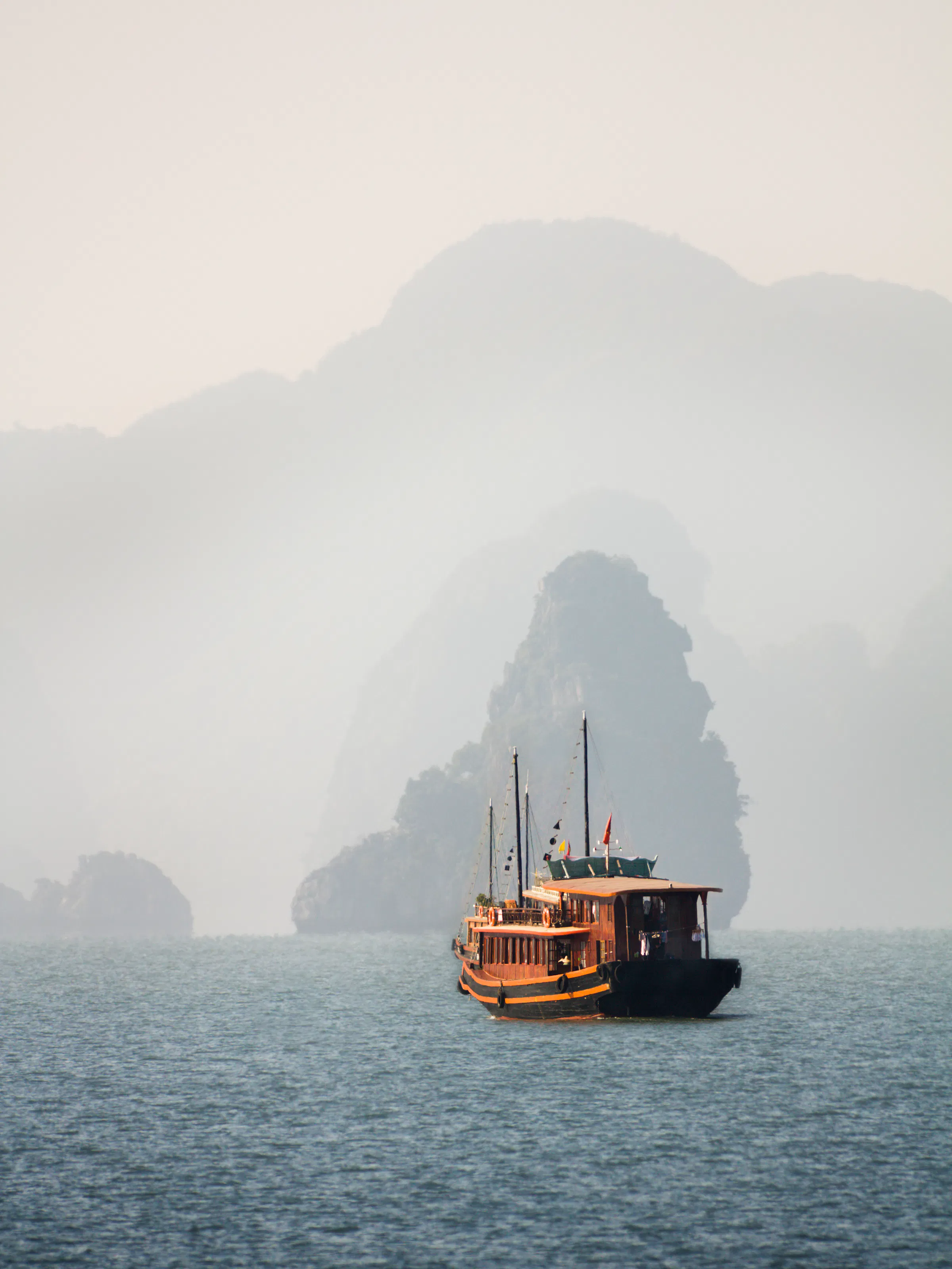 A large white cruise yacht anchors in still waters surrounded by limestone karsts in Ha Long Bay.