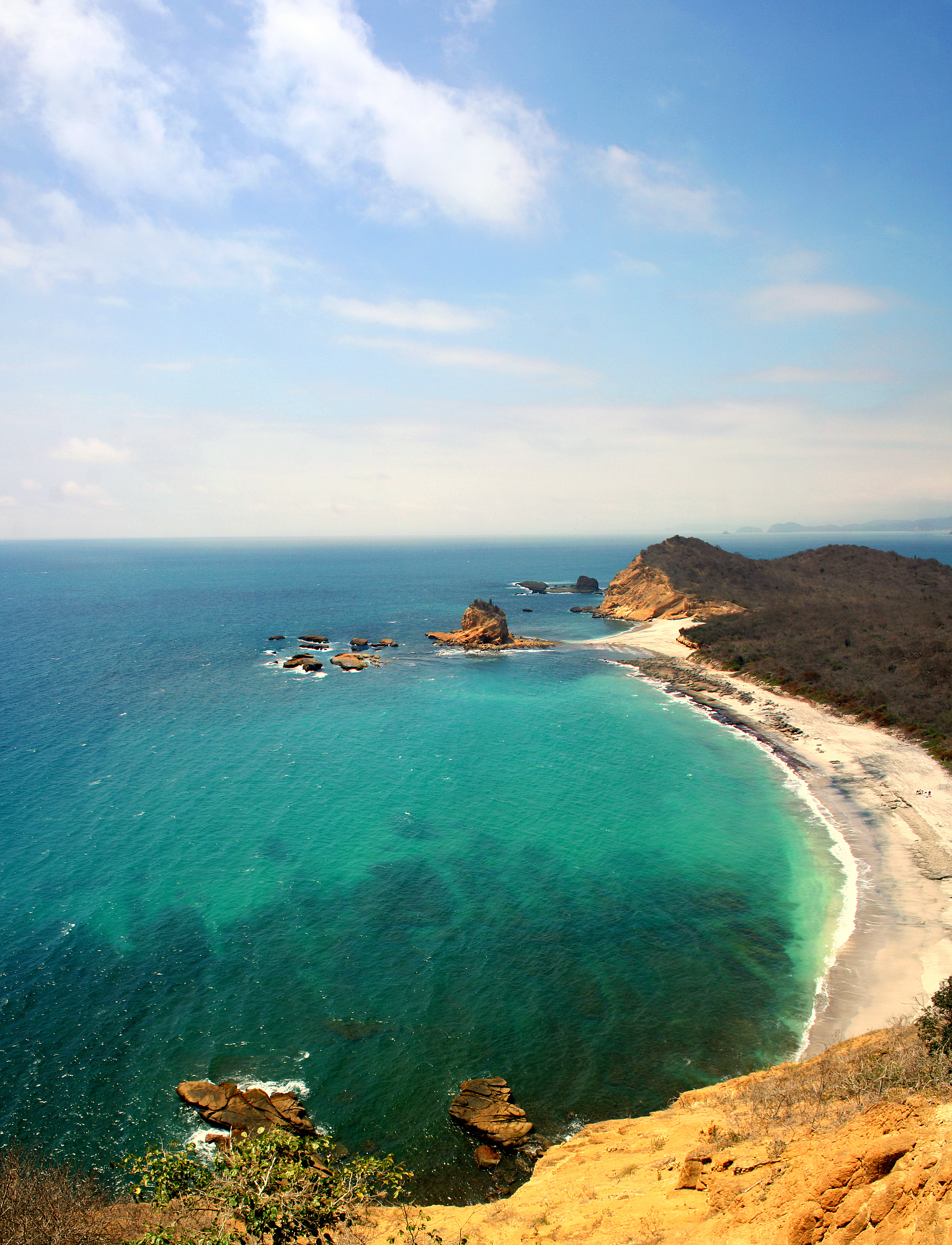 Rocky offshore islands rise from turquoise water with sandy beach visible at Machalilla, Ecuador.