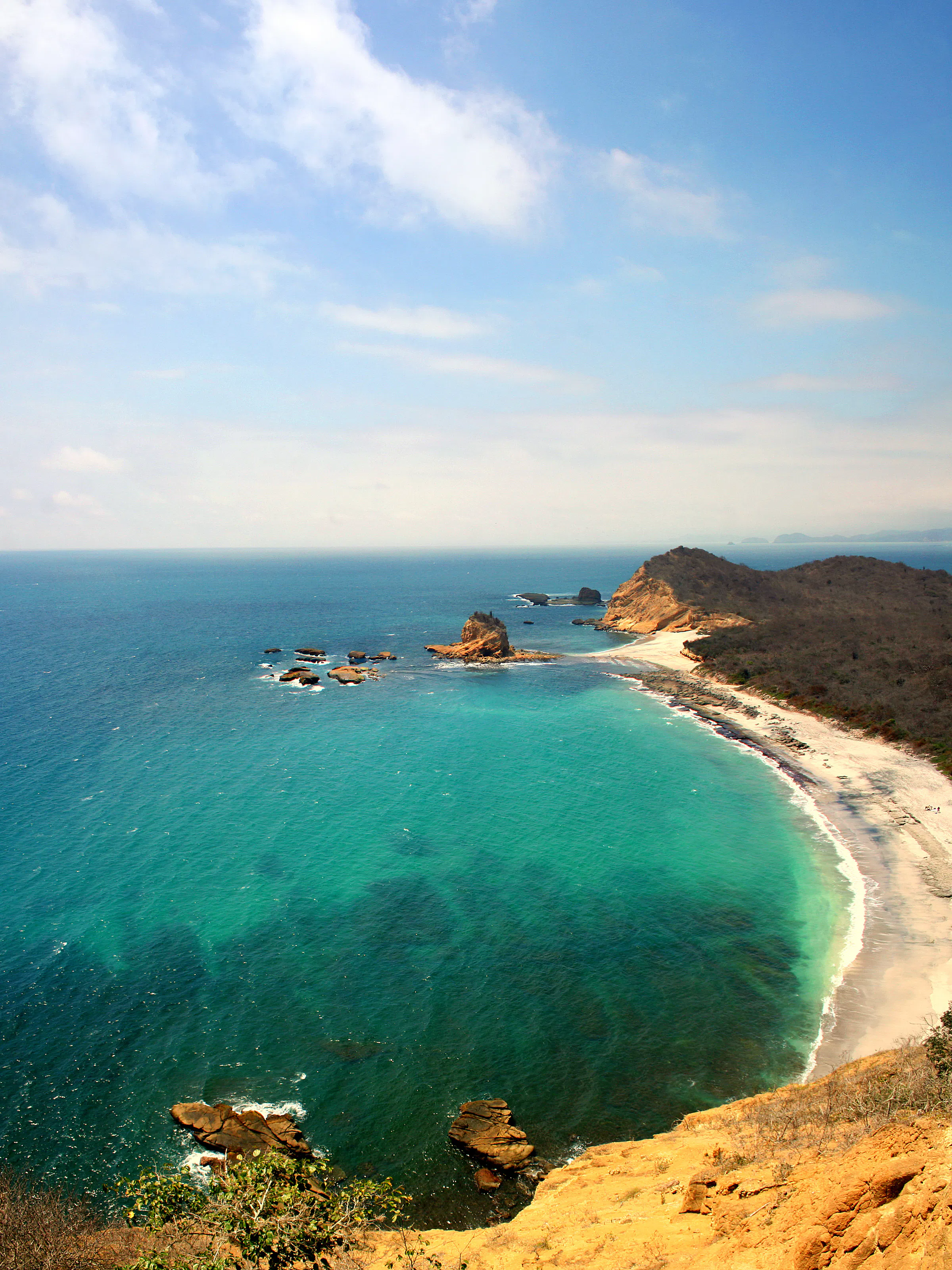 Rocky offshore islands rise from turquoise water with sandy beach visible at Machalilla, Ecuador.