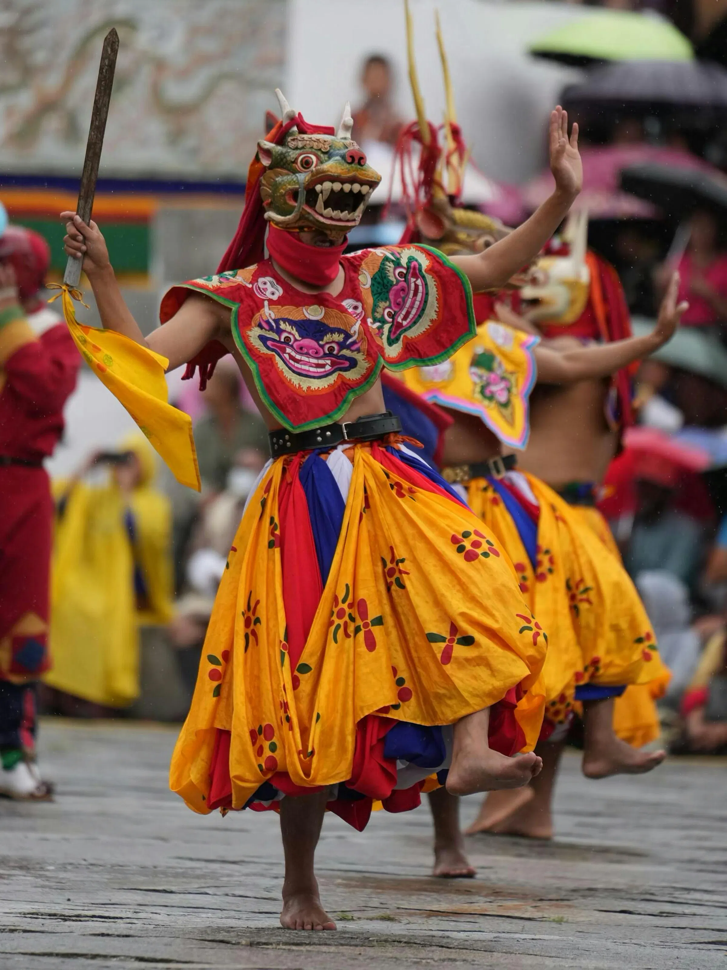 Costumed festival dancers in bright orange and red perform in the courtyard of a Bhutanese dzong.