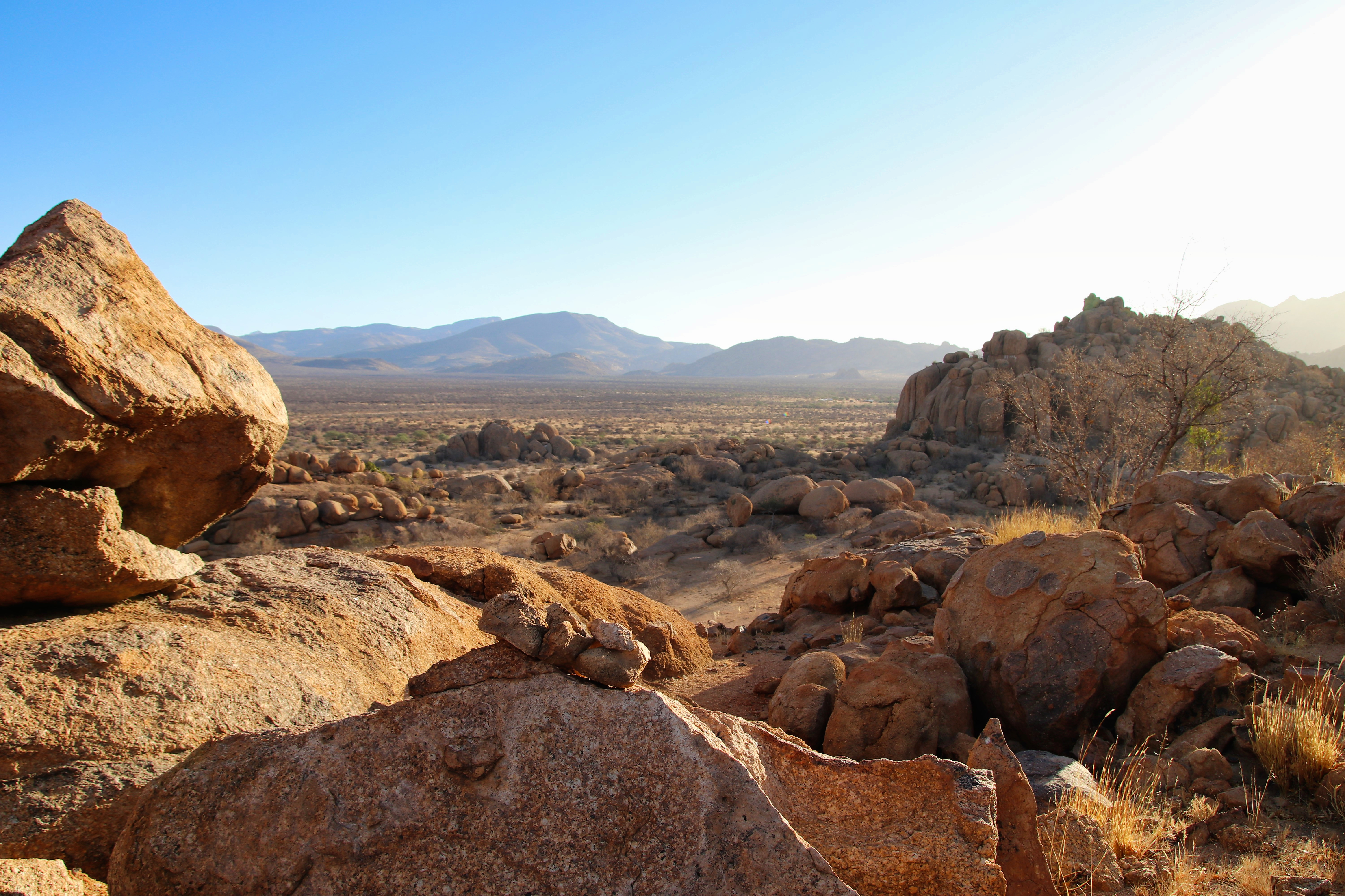 Smooth orange sandstone boulders are stacked in an arid landscape under a blue sky near Windhoek.