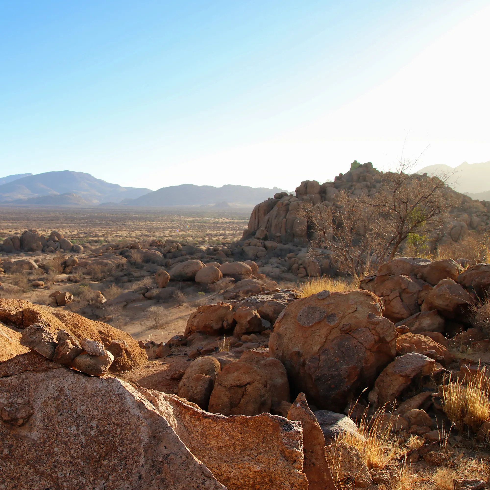 Smooth orange sandstone boulders are stacked in an arid landscape under a blue sky near Windhoek.
