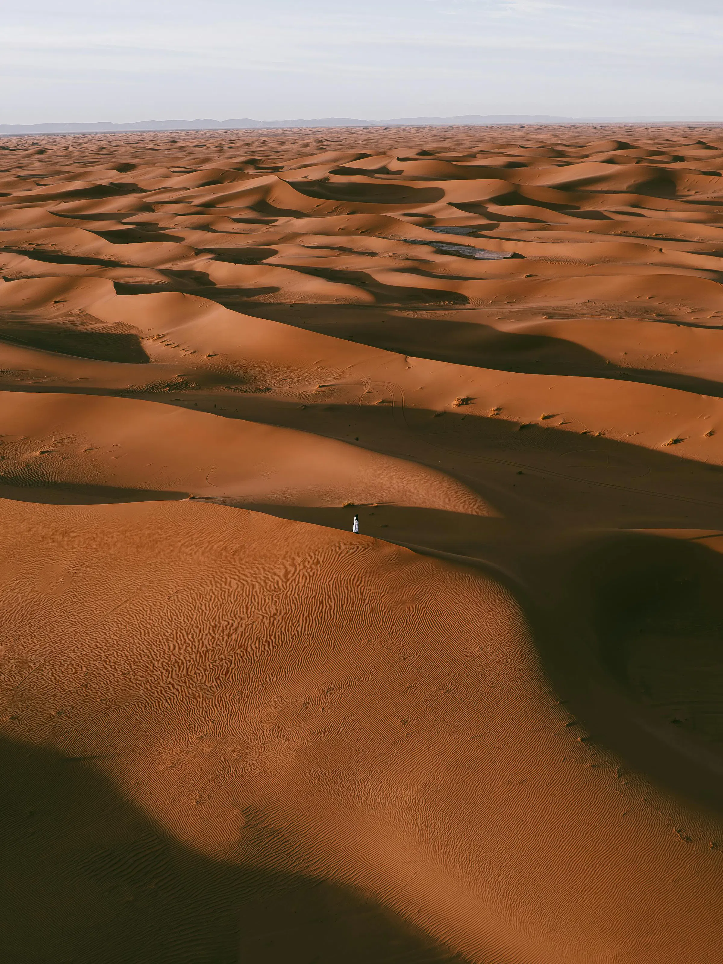 Tall orange and red sand dunes stretch to the horizon under a deep blue sky in Morocco's Sahara.