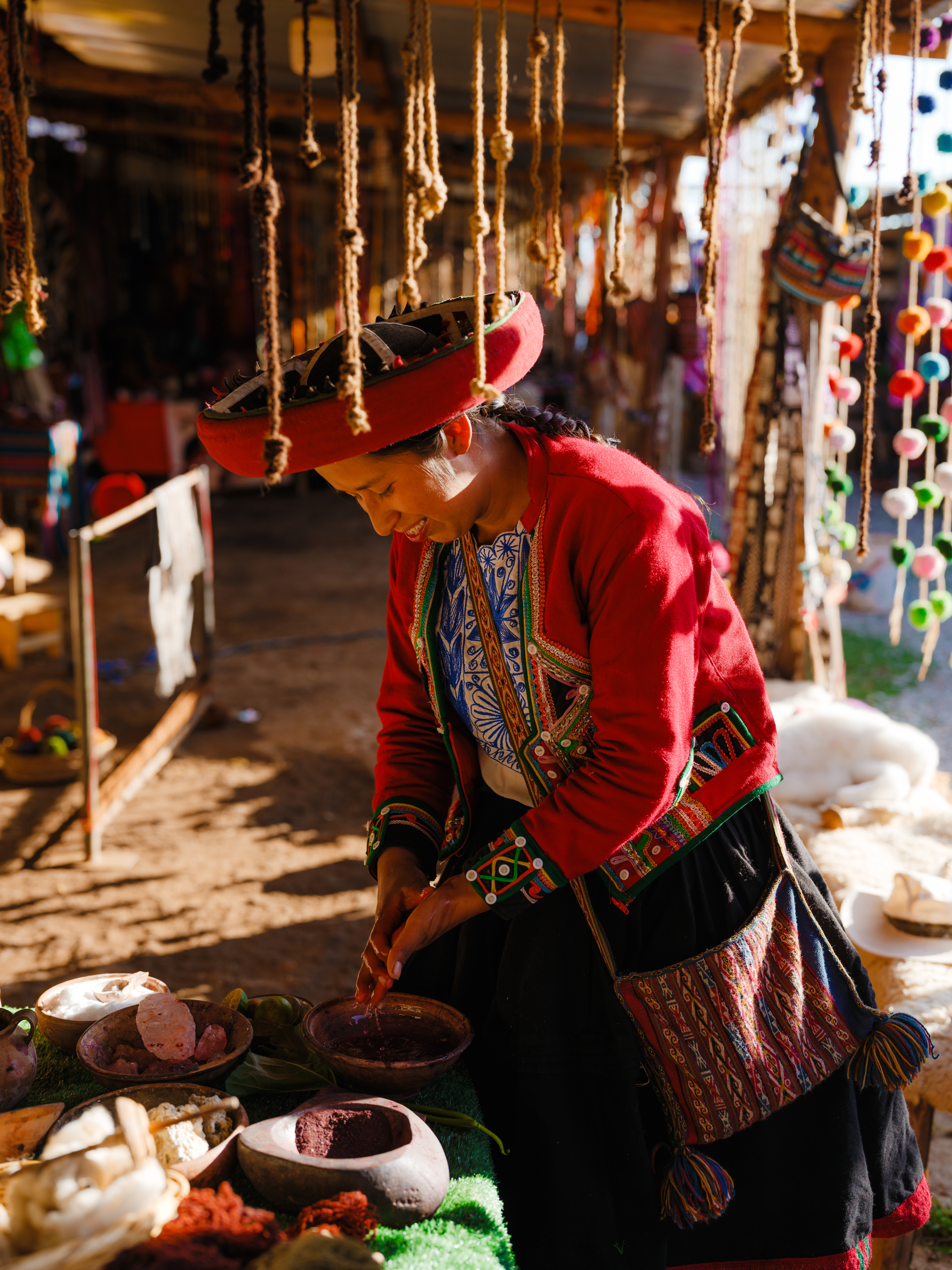 An indigenous woman in traditional red clothing works with natural dye at a Peruvian highland market.