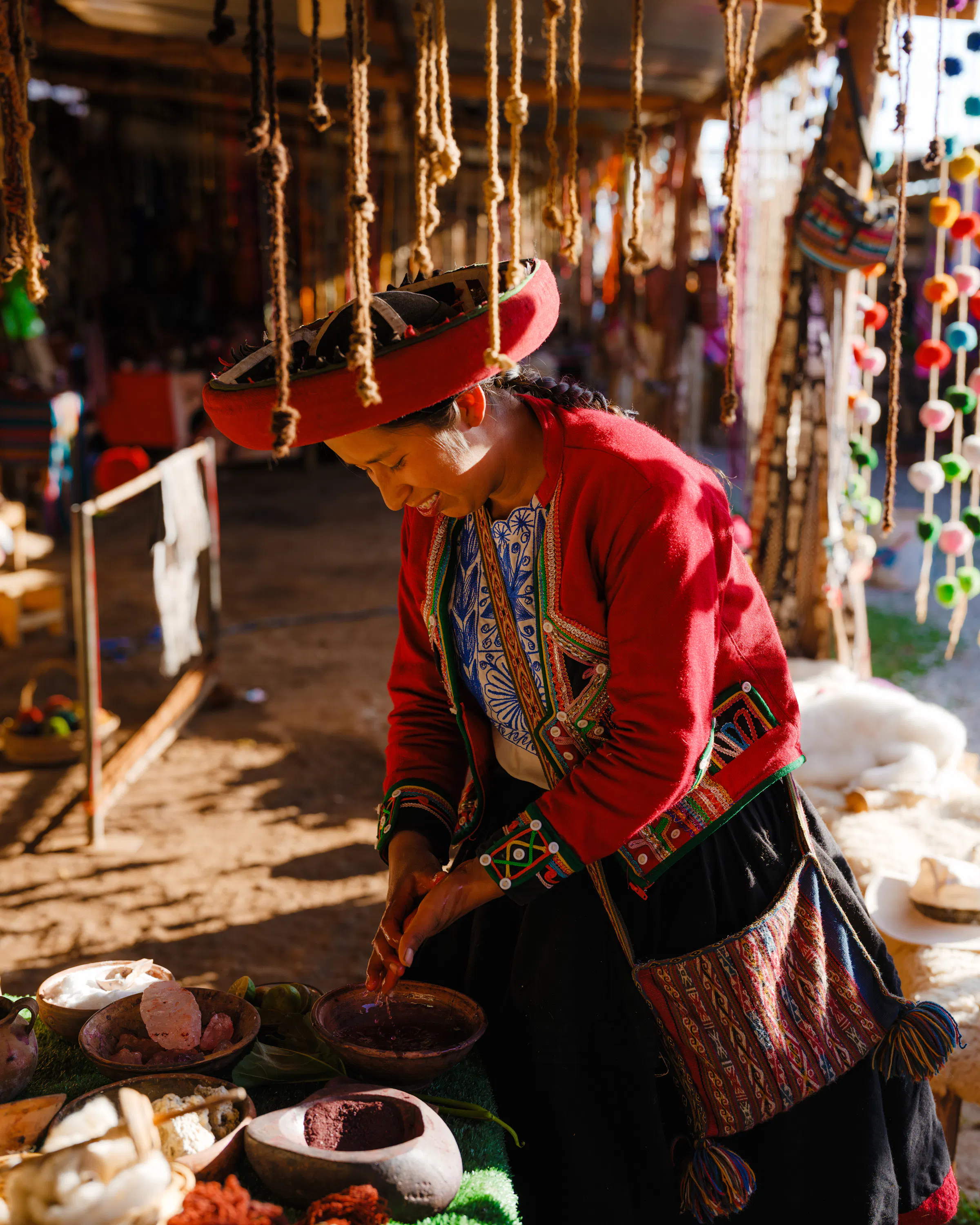 An indigenous woman in traditional red clothing works with natural dye at a Peruvian highland market.
