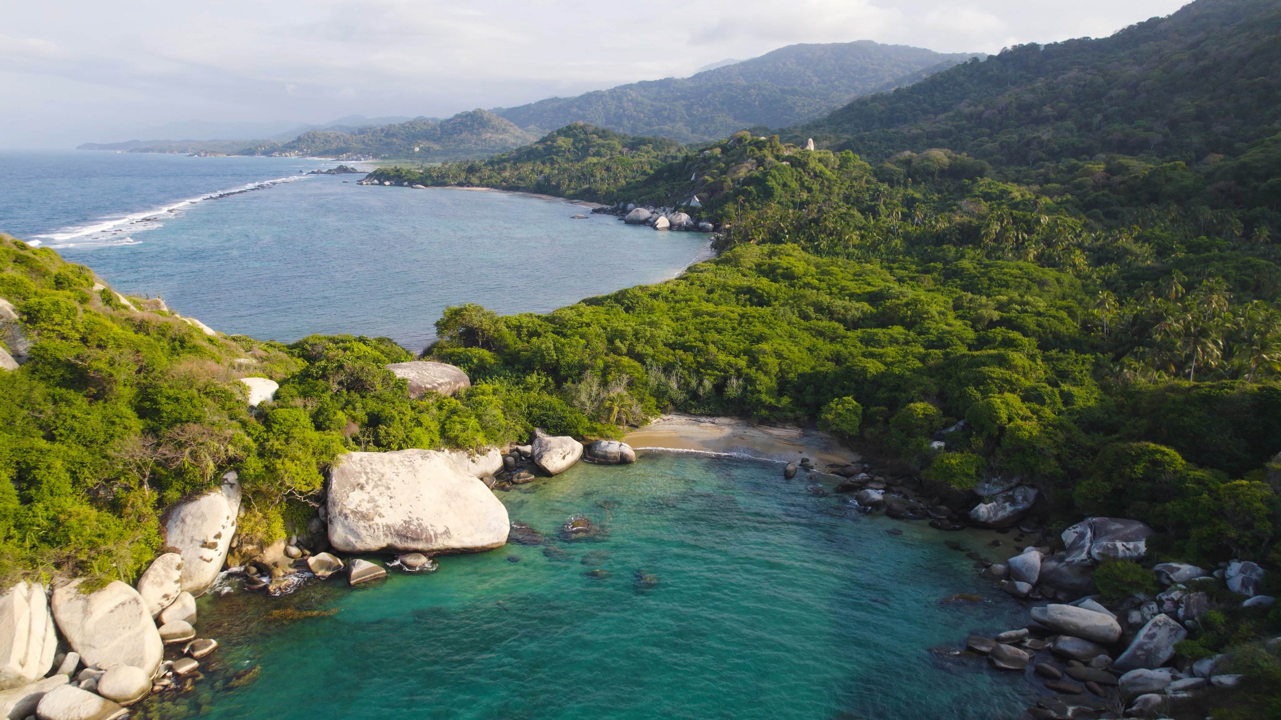 Aerial view of jungle cliffs meeting turquoise Caribbean water at Cabo San Juan, Tayrona Park.