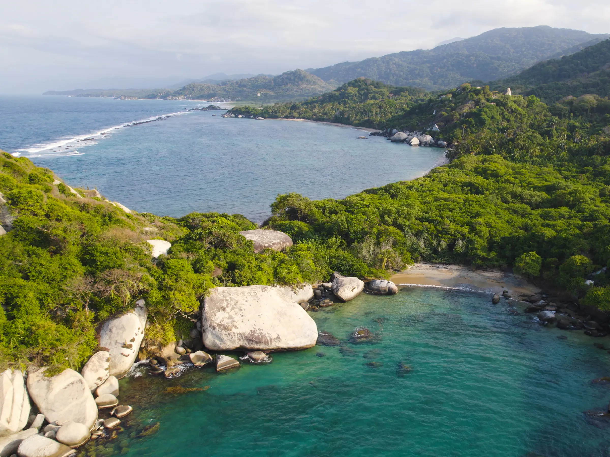 Aerial view of jungle cliffs meeting turquoise Caribbean water at Cabo San Juan, Tayrona Park.