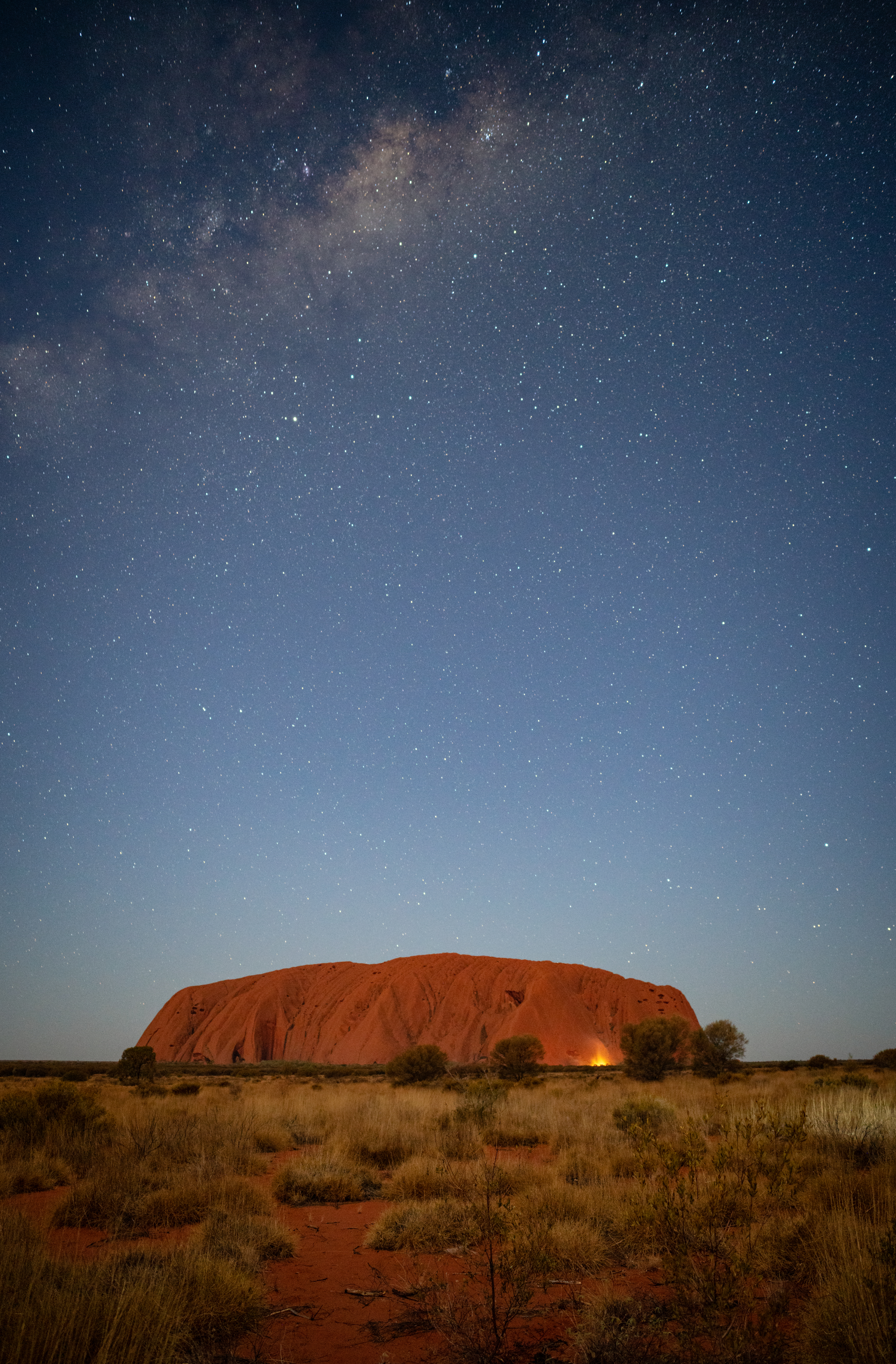 Uluru rises as a massive dark silhouette against a star-filled night sky in Australia's Red Centre.