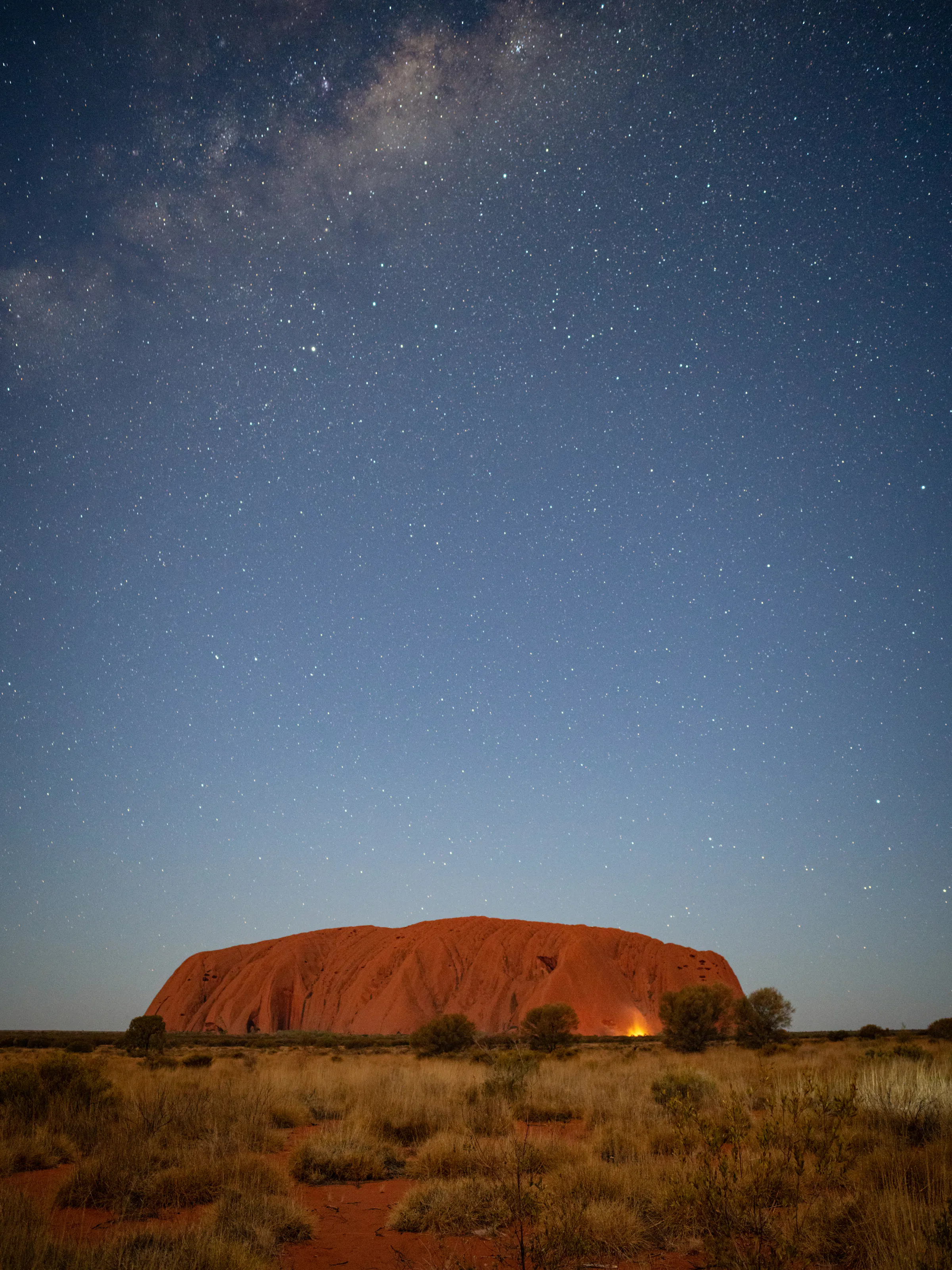 Uluru rises as a massive dark silhouette against a star-filled night sky in Australia's Red Centre.
