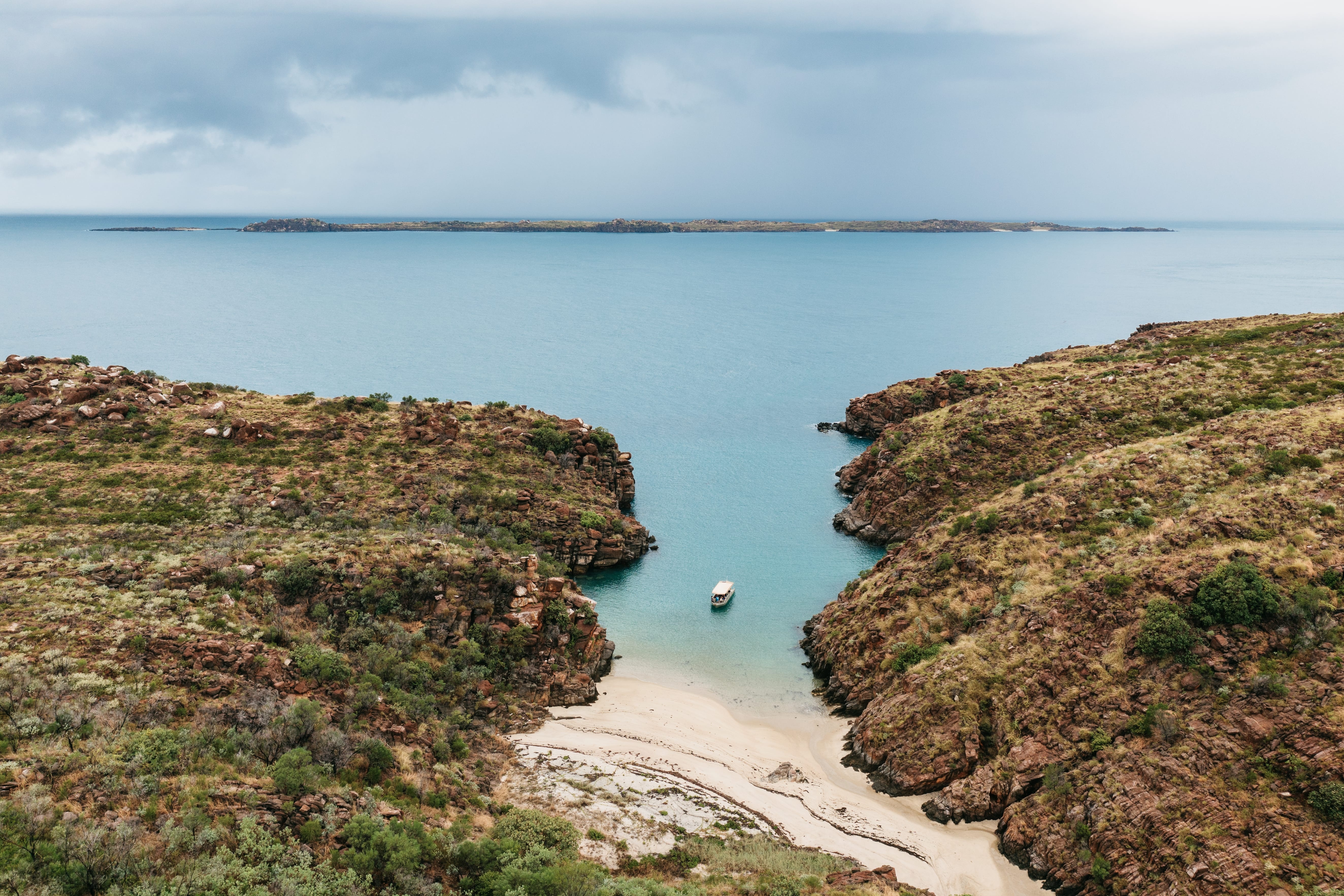 A group of surfers and swimmers gather in the shallows of a wide curved bay in Australia.