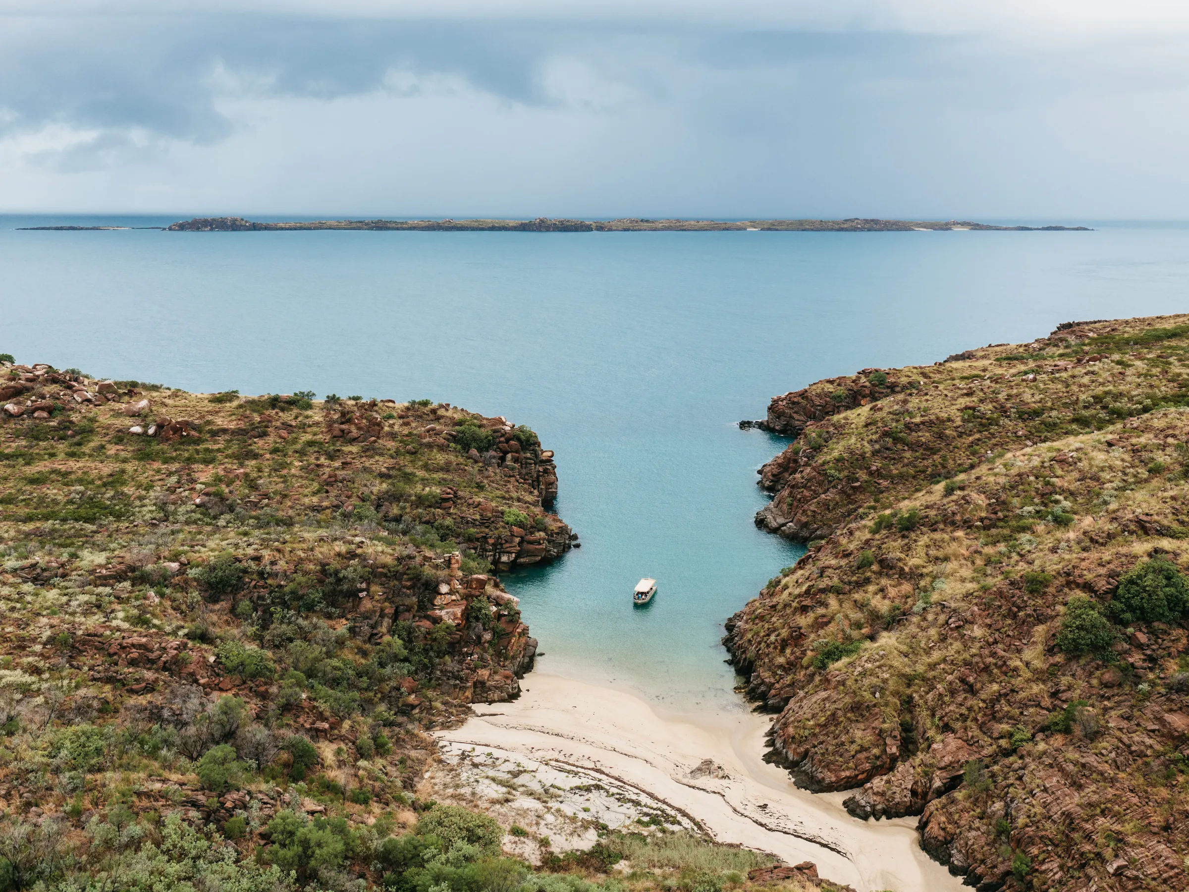 A group of surfers and swimmers gather in the shallows of a wide curved bay in Australia.