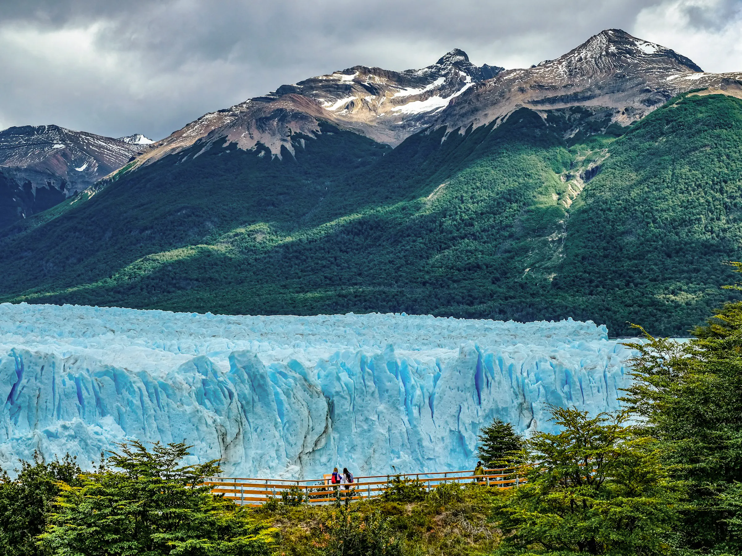 The deep blue ice face of Perito Moreno Glacier stretches wide with Andean peaks rising behind.