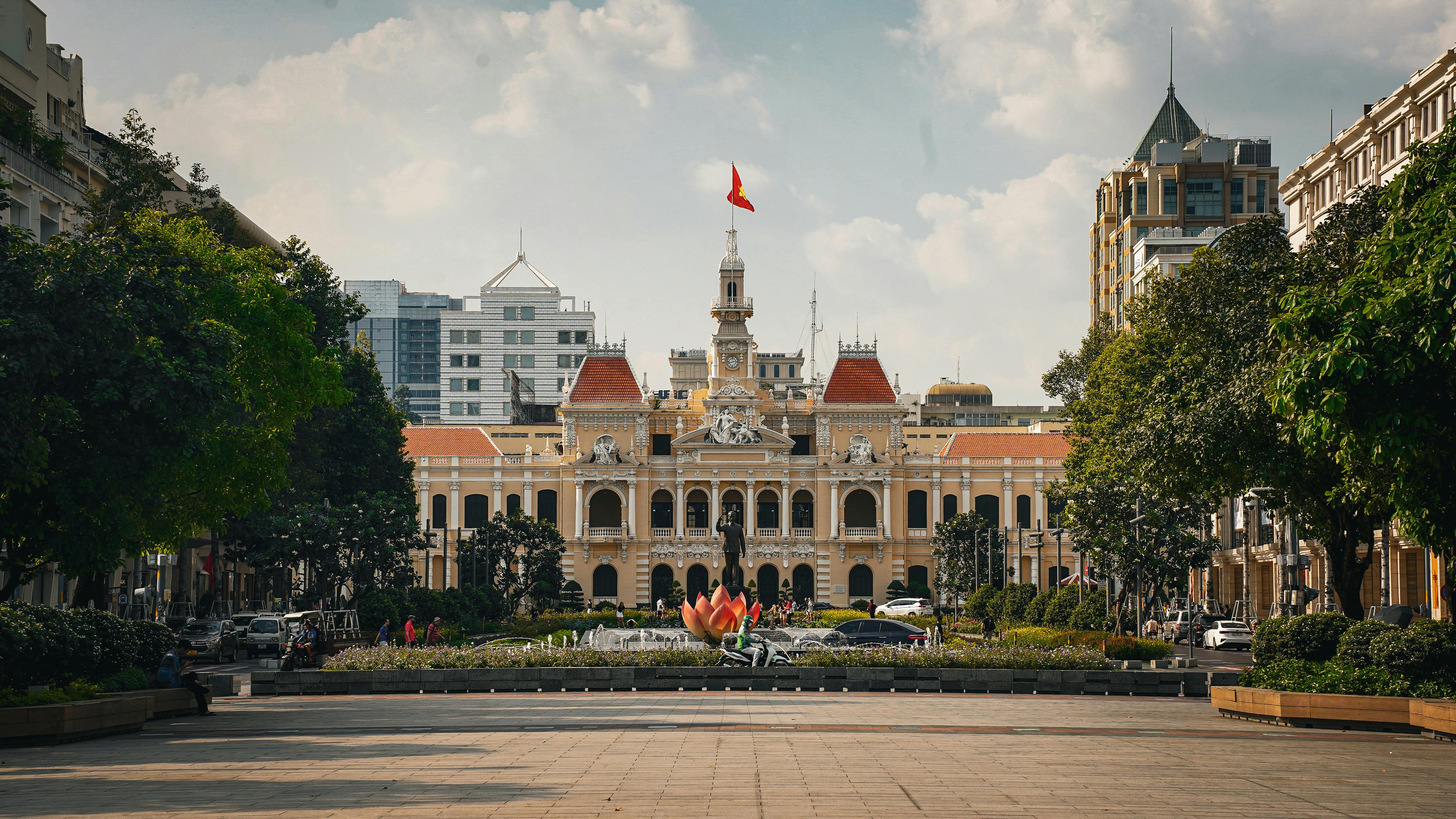 Ho Chi Minh City's colonial-era town hall is illuminated at night with motorbikes passing in front.