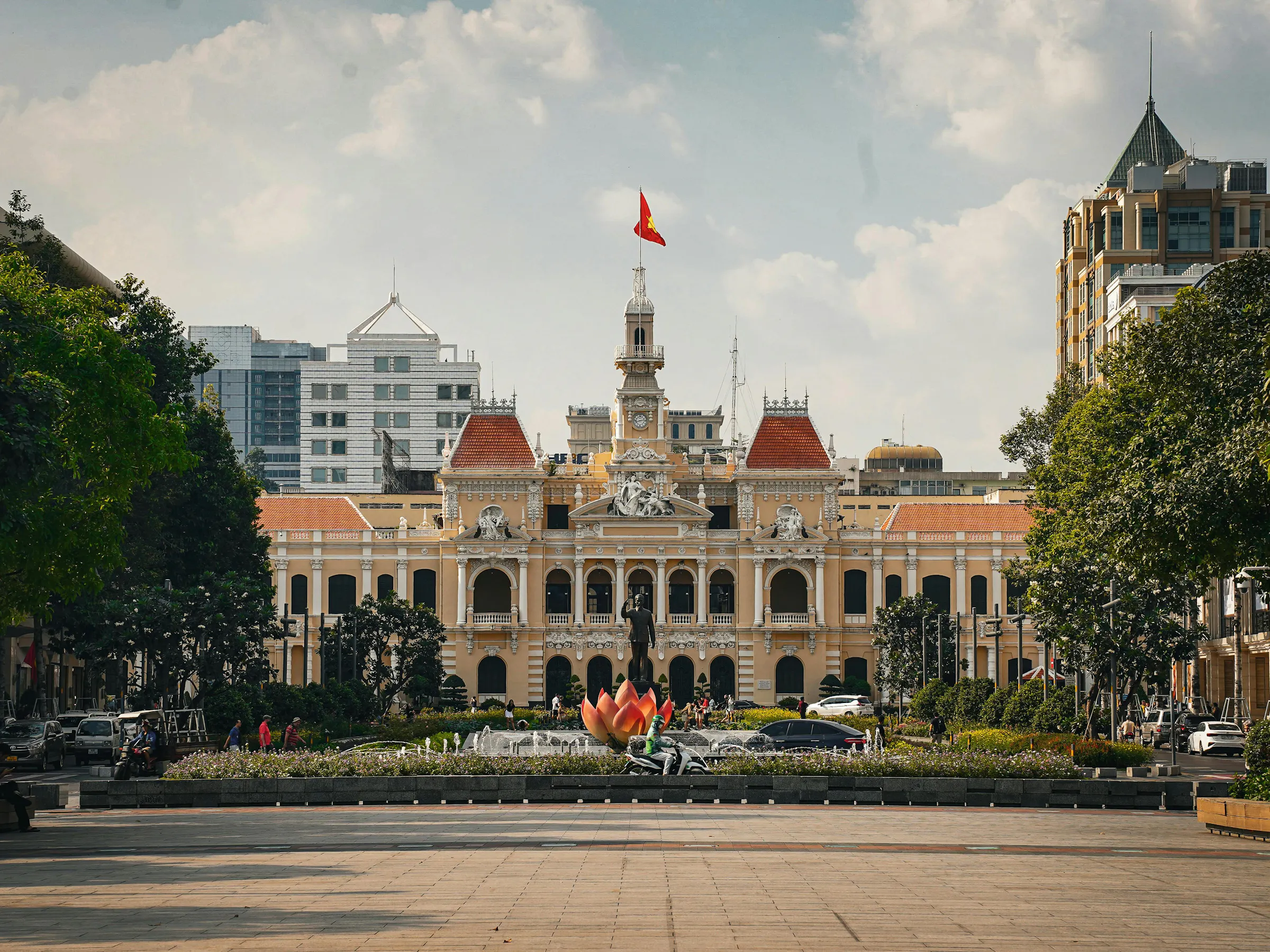 Ho Chi Minh City's colonial-era town hall is illuminated at night with motorbikes passing in front.