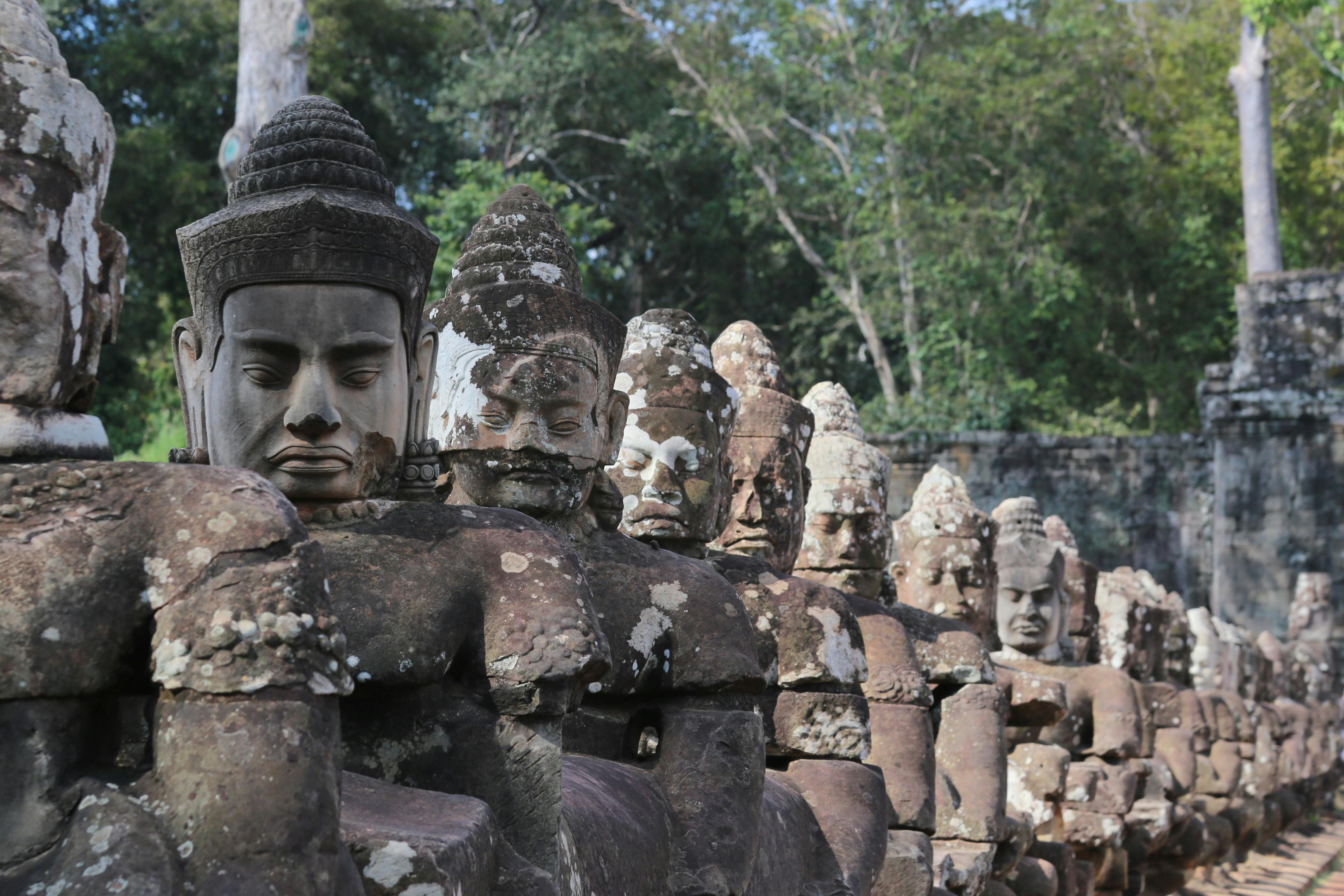 Large stone face carvings on a moss-covered Bayon temple tower gaze outward in Angkor, Cambodia.