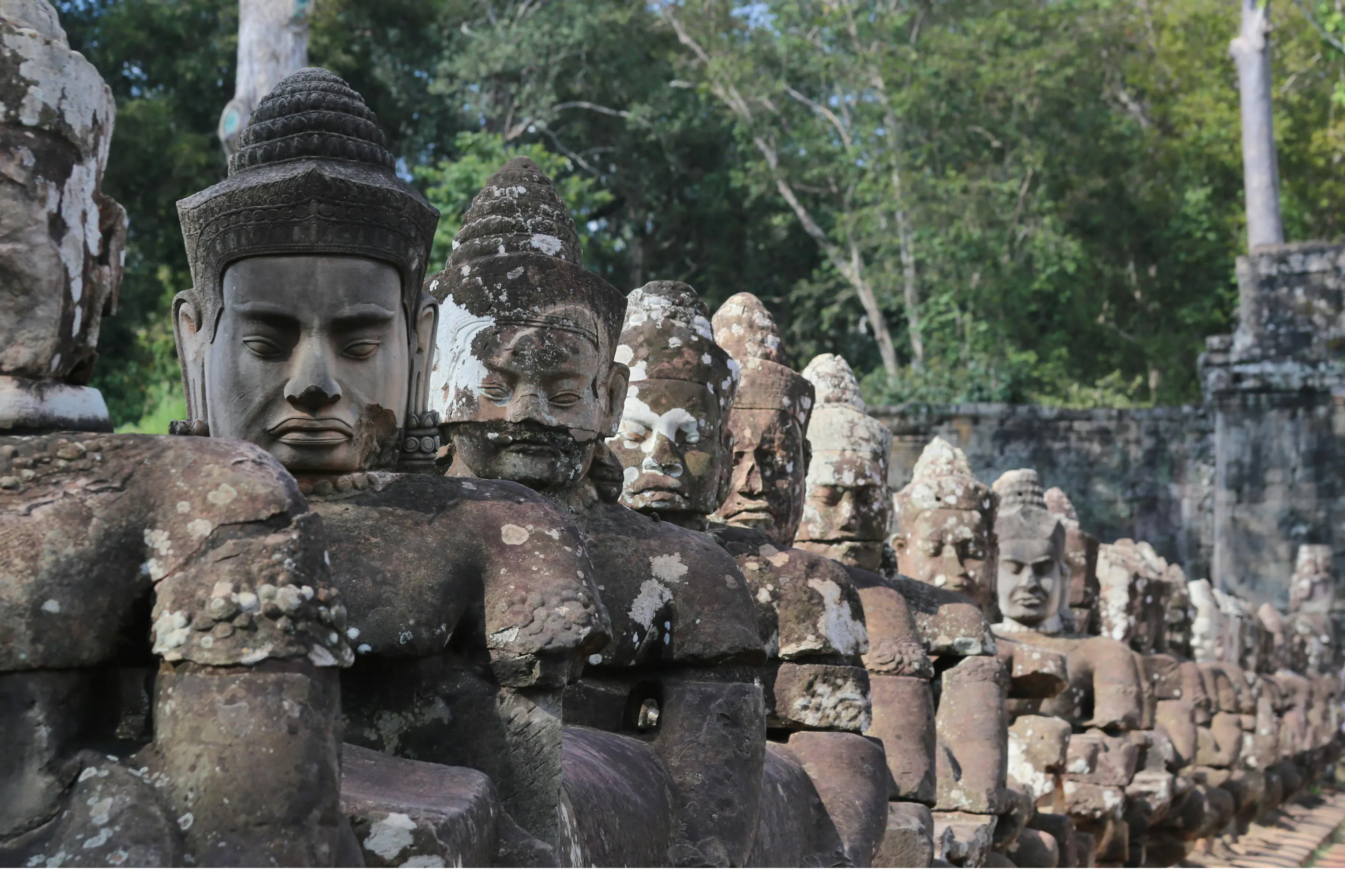 Large stone face carvings on a moss-covered Bayon temple tower gaze outward in Angkor, Cambodia.