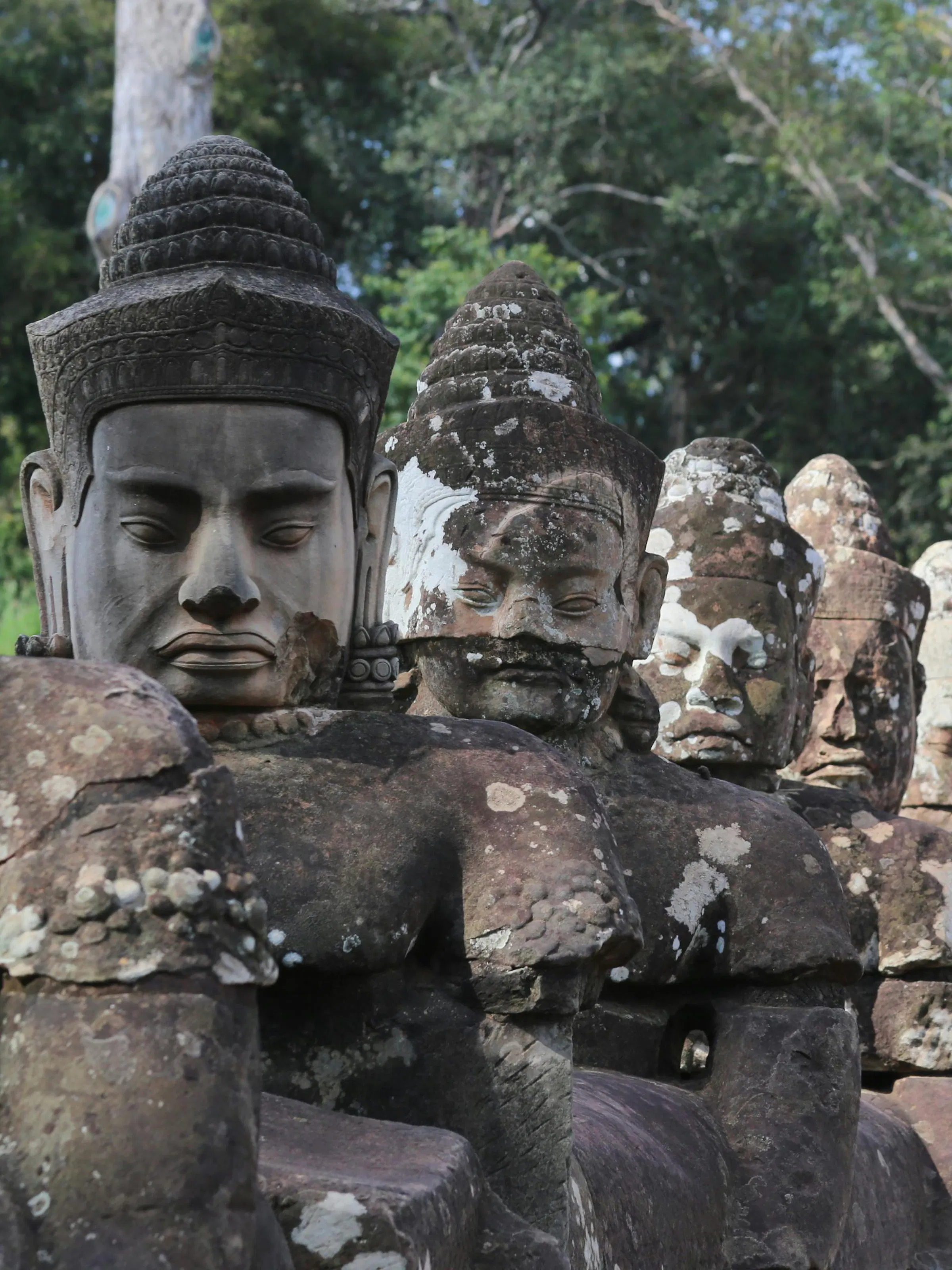 Large stone face carvings on a moss-covered Bayon temple tower gaze outward in Angkor, Cambodia.