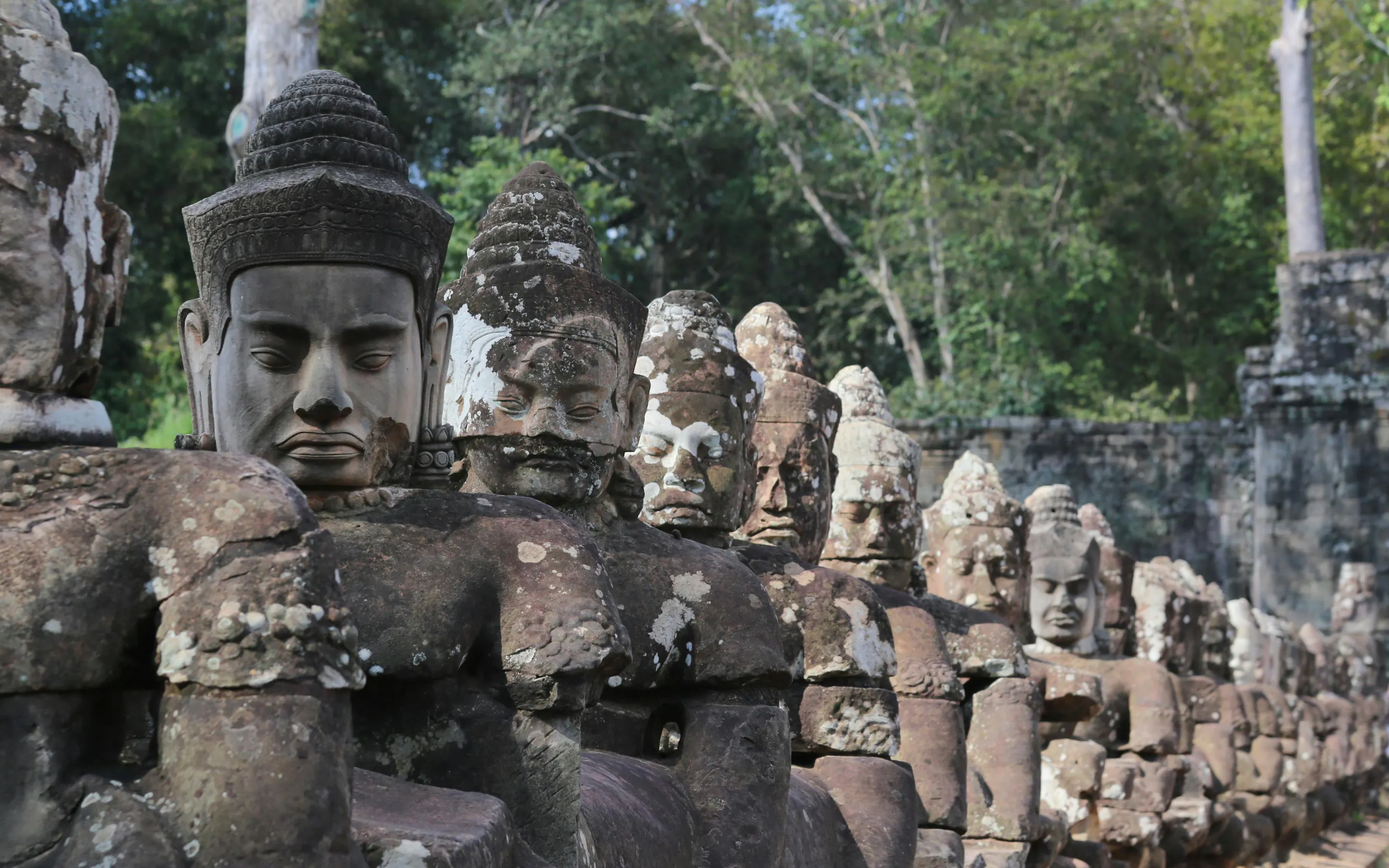 Large stone face carvings on a moss-covered Bayon temple tower gaze outward in Angkor, Cambodia.