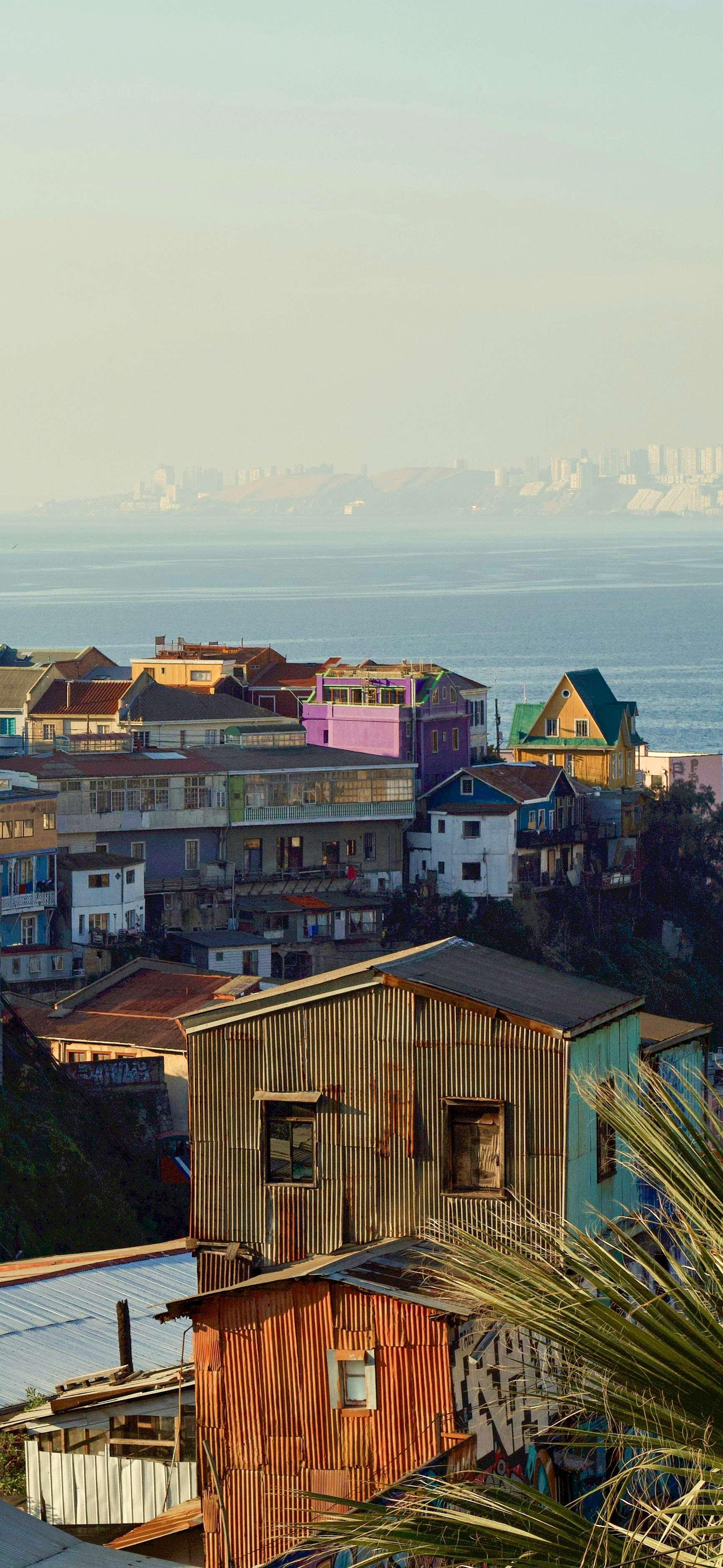 A steeply sloped street in Valparaíso is lined with brightly painted houses in yellow and pink.