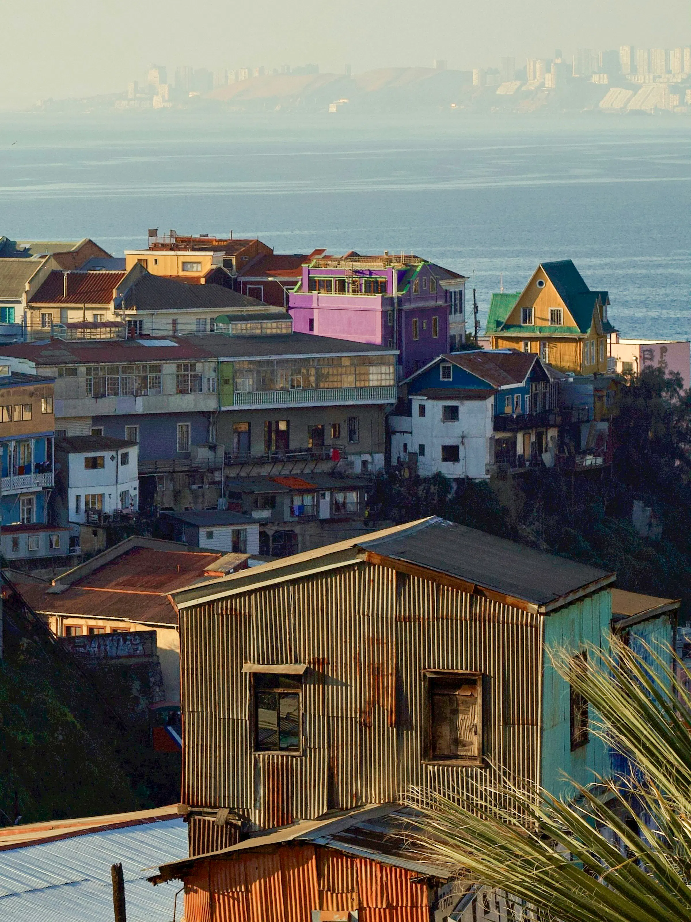 A steeply sloped street in Valparaíso is lined with brightly painted houses in yellow and pink.
