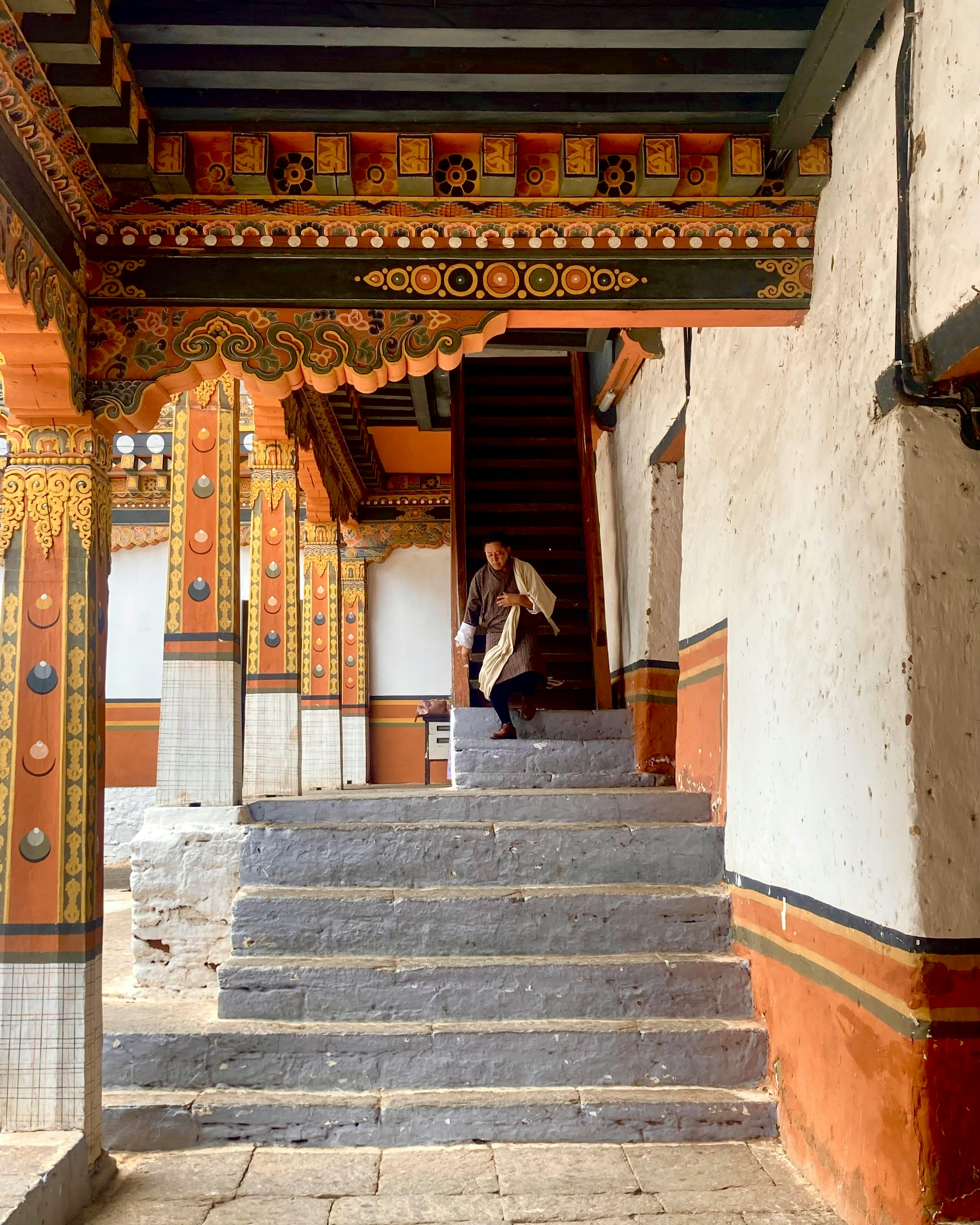 A traditional Bhutanese dzong with white-washed walls and a red roof is set into a steep hillside.