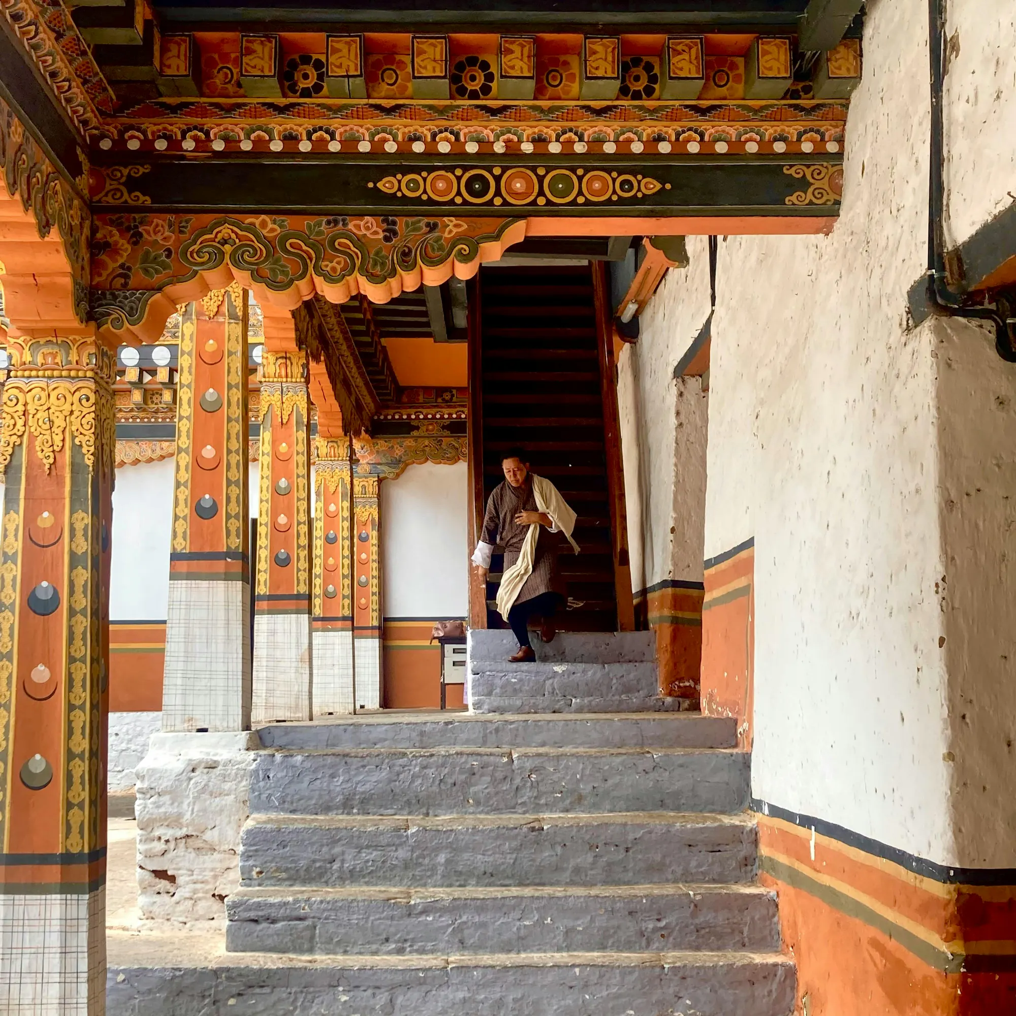 A traditional Bhutanese dzong with white-washed walls and a red roof is set into a steep hillside.