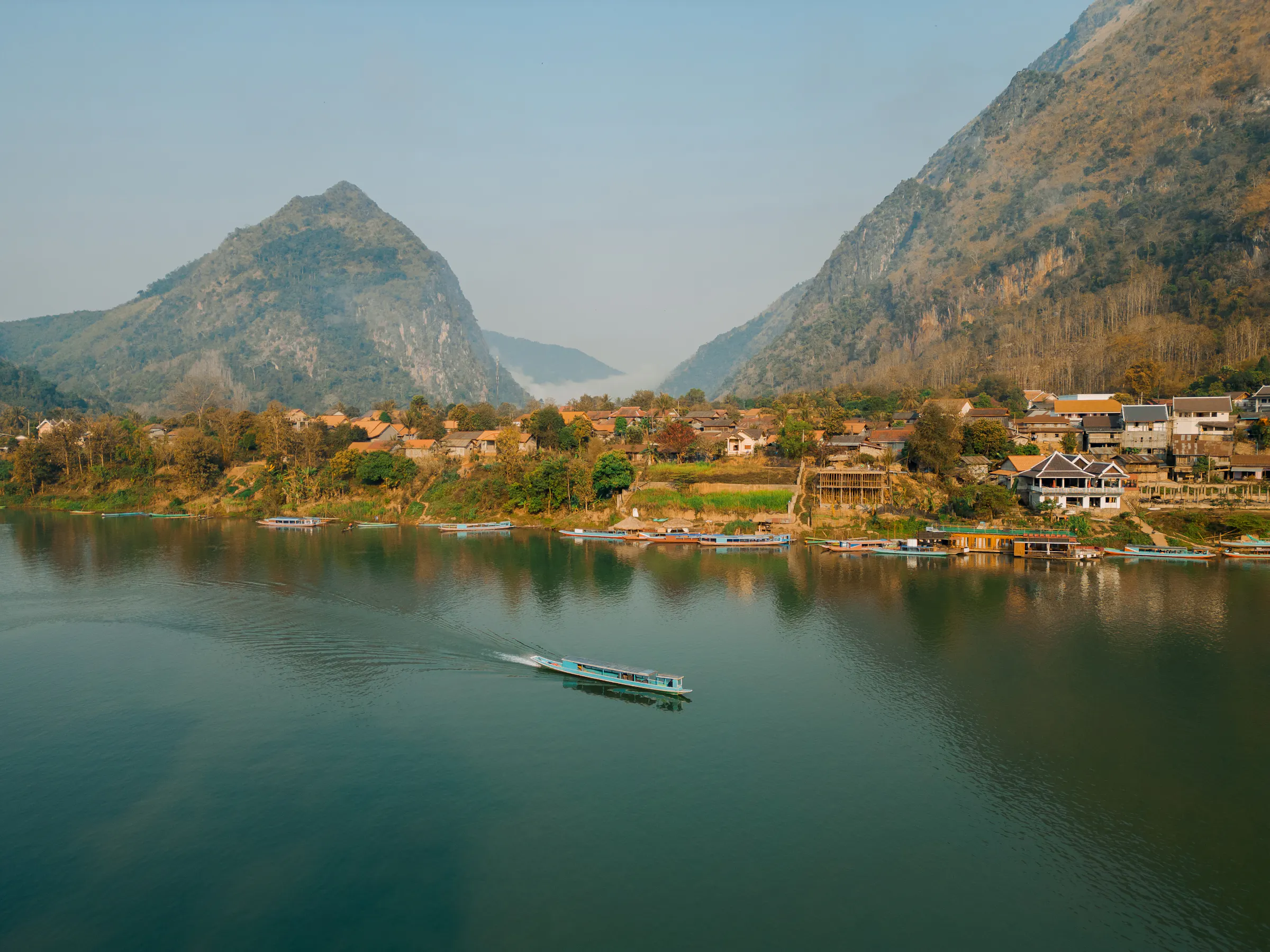 A calm river reflects karst limestone peaks and lush green hills at dusk in Vang Vieng, Laos.