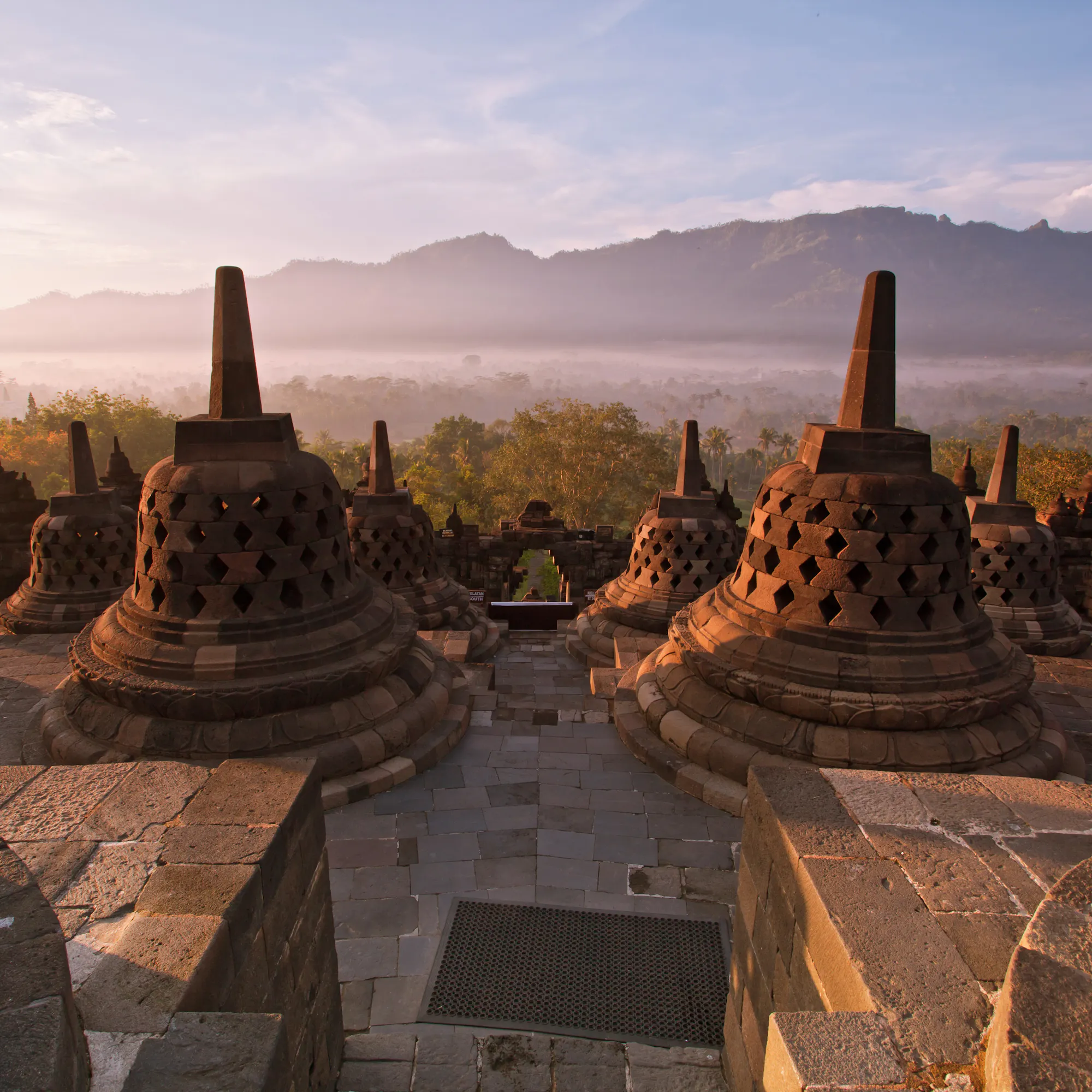 The stone stupas and terraces of Borobudur temple glow in warm morning light in central Java.