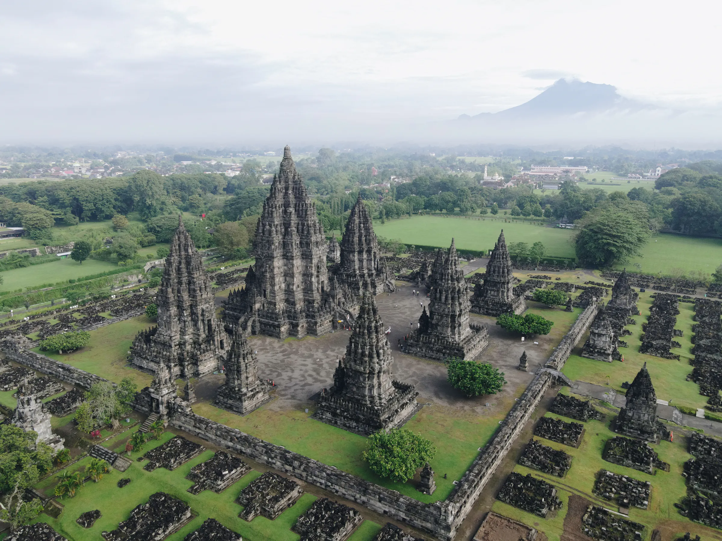 Aerial view of Prambanan Hindu temple complex with tall spires rising from a green Java landscape.