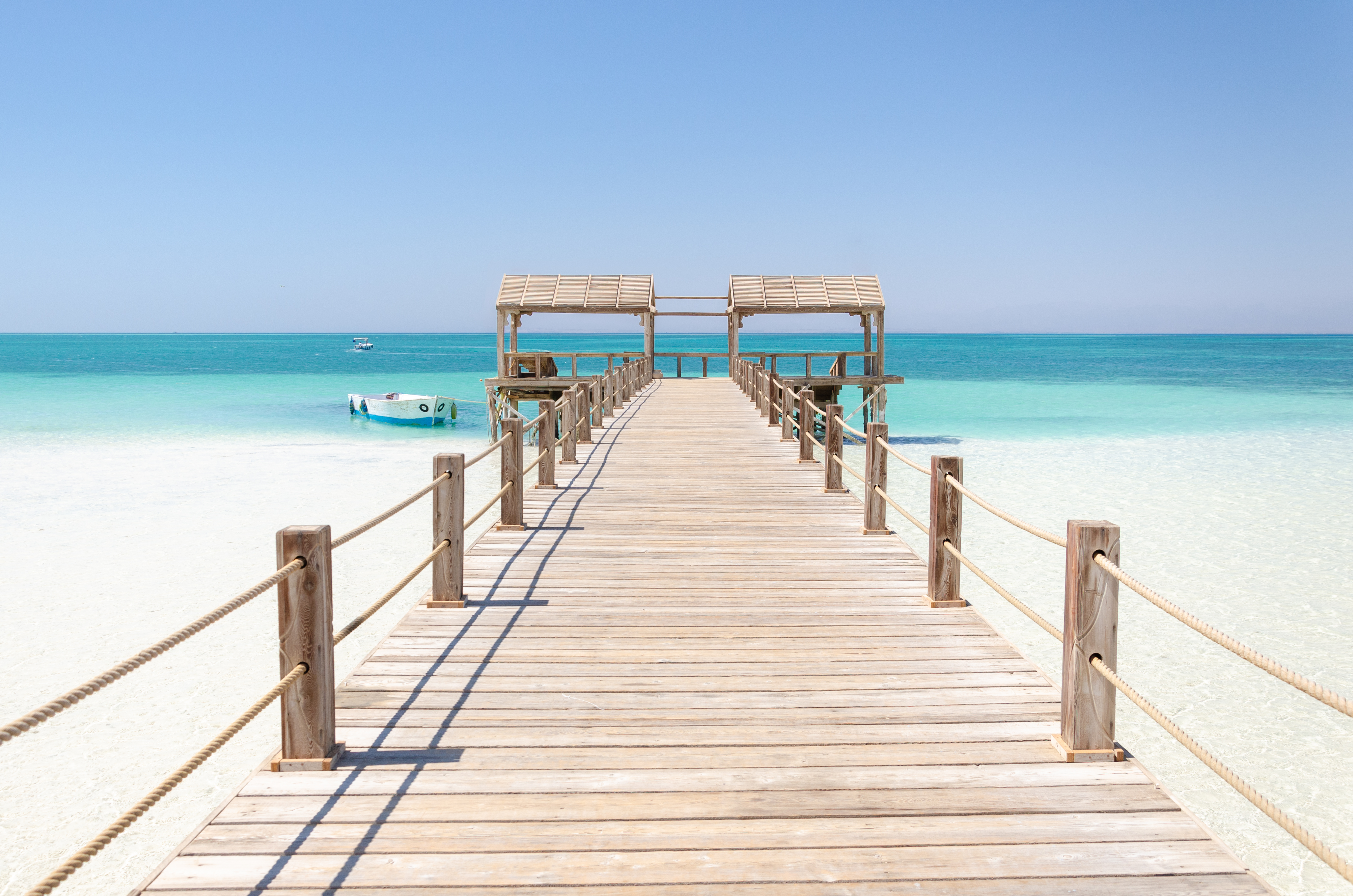 A wooden pier stretches over calm shallow turquoise water toward the open Red Sea.