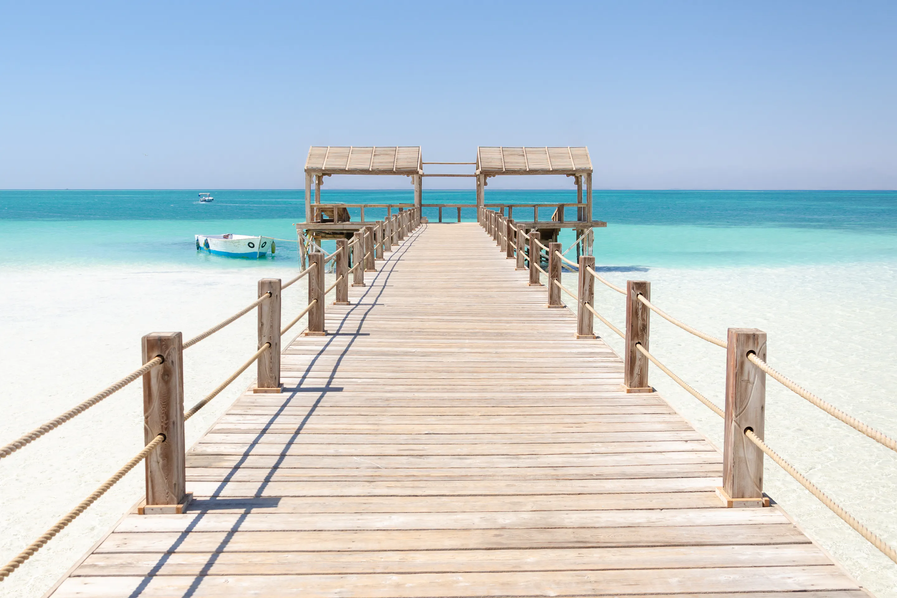 A wooden pier stretches over calm shallow turquoise water toward the open Red Sea.