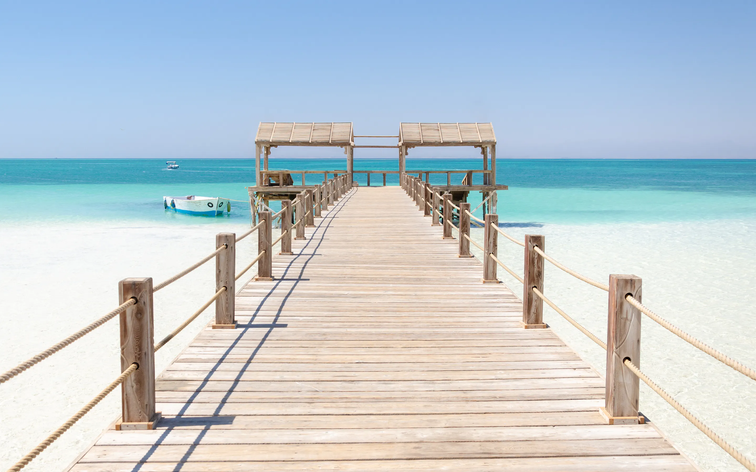 A wooden pier stretches over calm shallow turquoise water toward the open Red Sea.