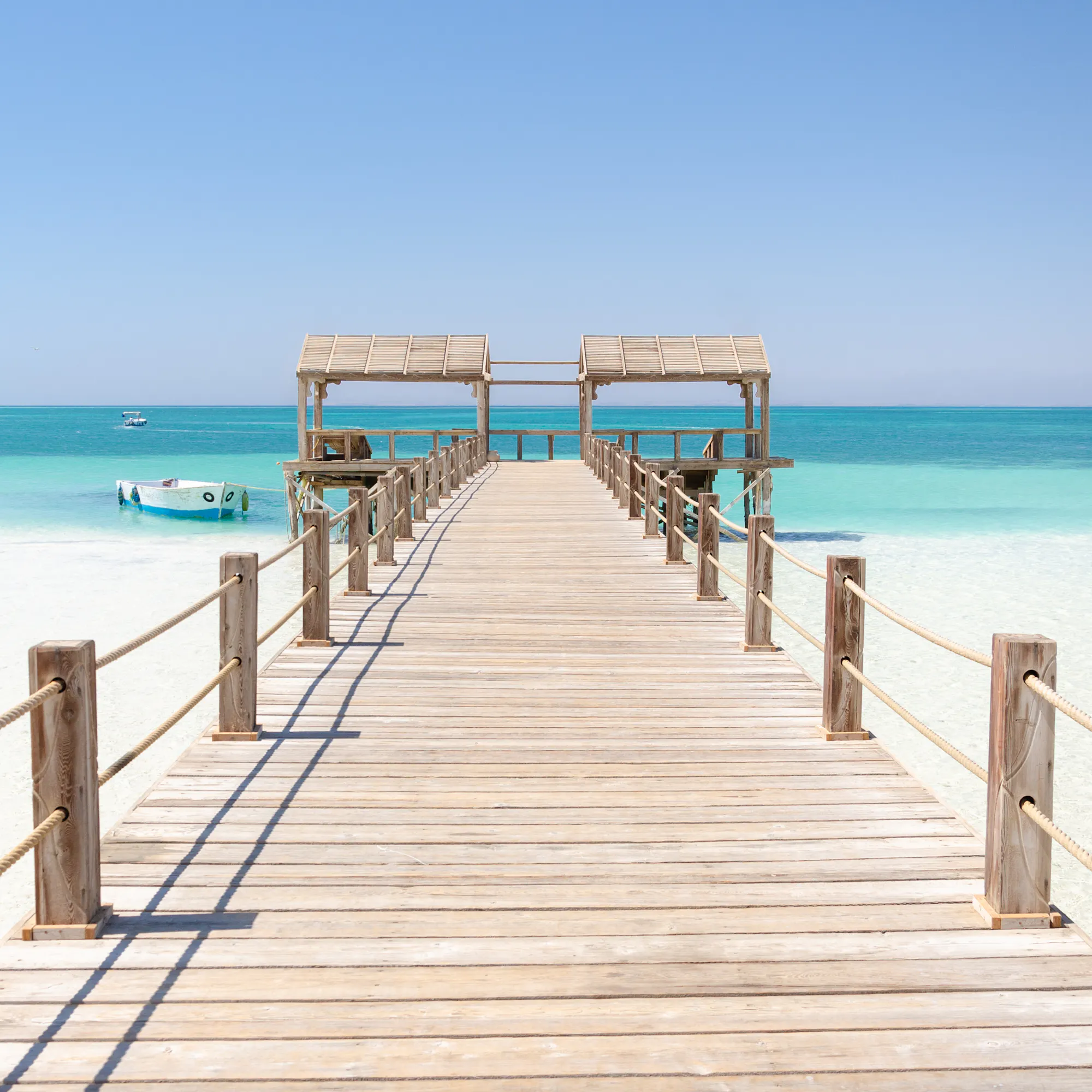 A wooden pier stretches over calm shallow turquoise water toward the open Red Sea.