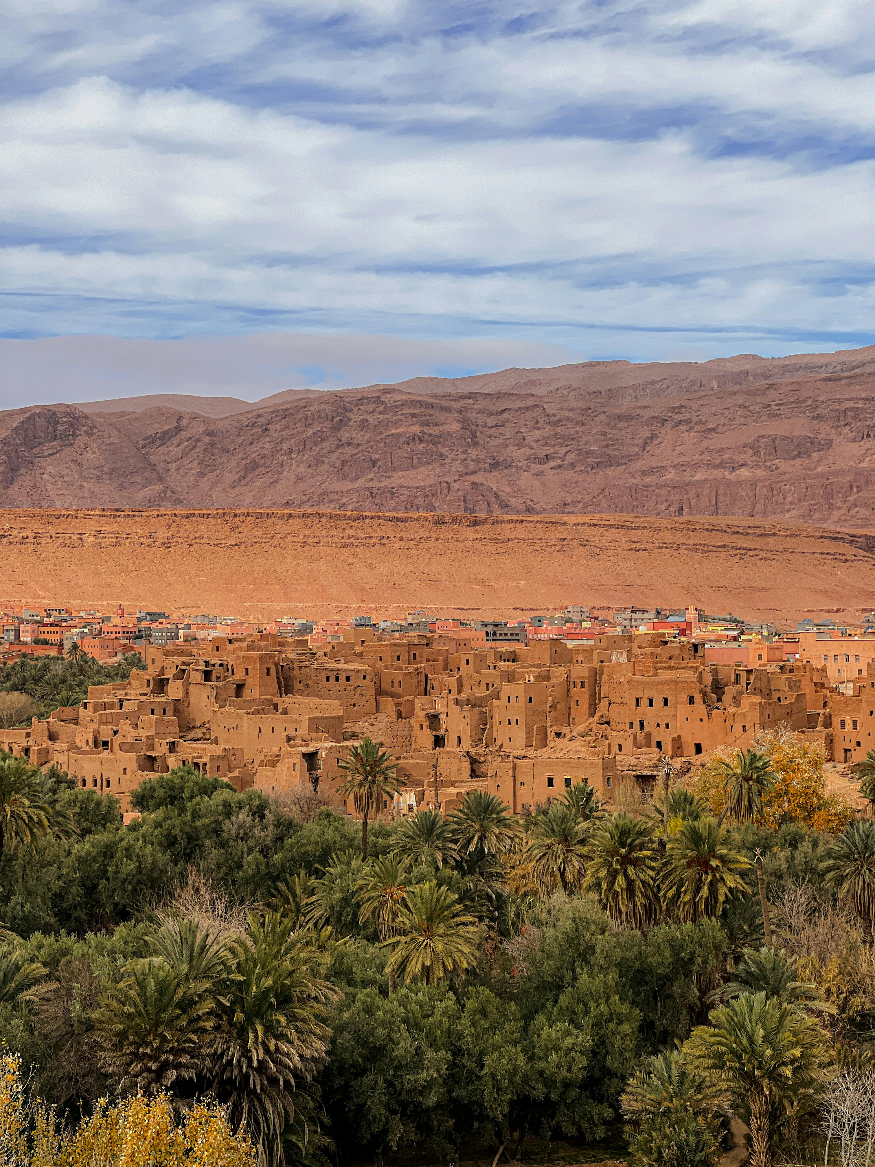 A mud-brick kasbah rises above a sparse desert landscape with low hills and dry scrub in Ouarzazate.