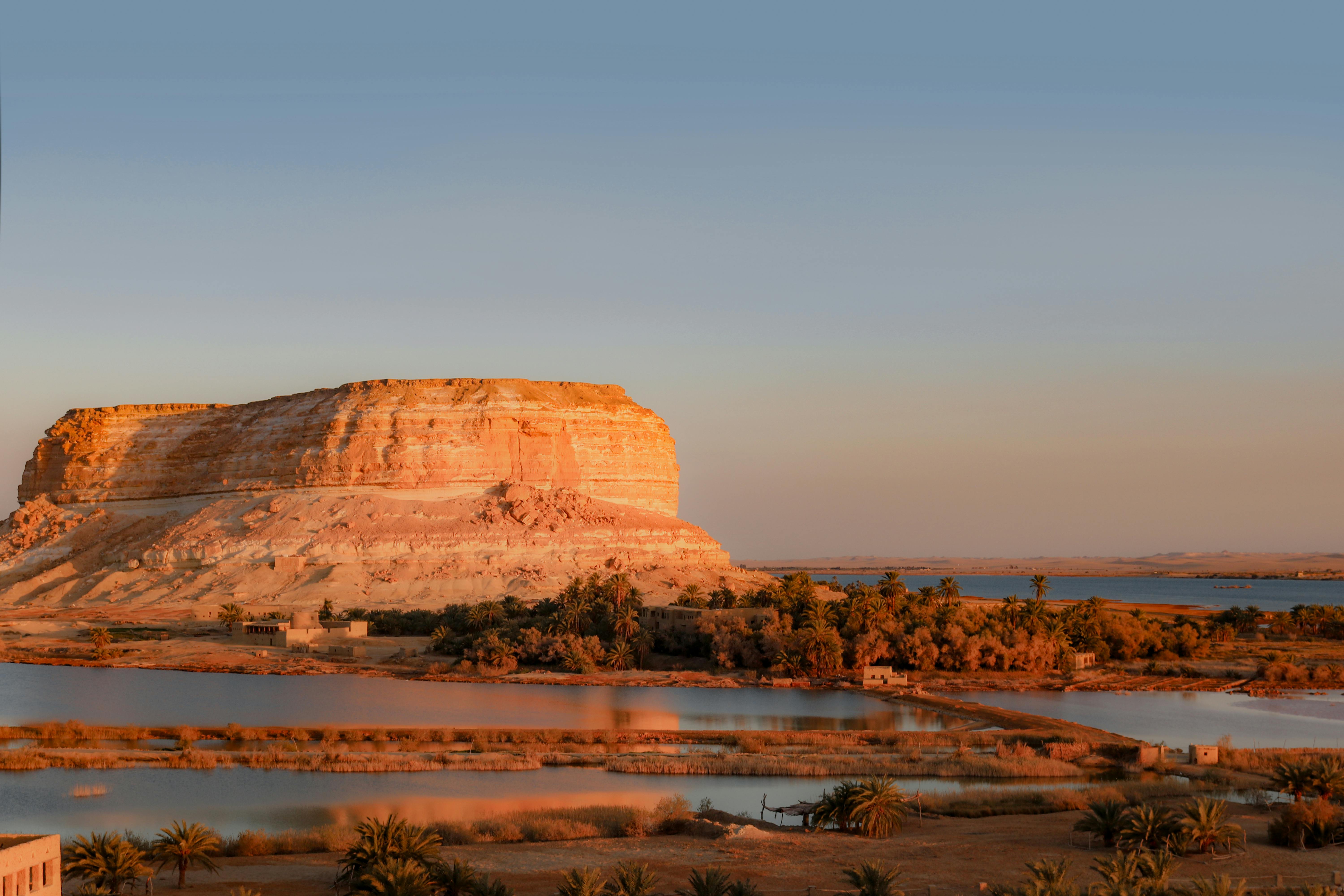 A flat desert mesa rises above a shallow lake and arid plain in the Siwa Oasis region of Egypt.