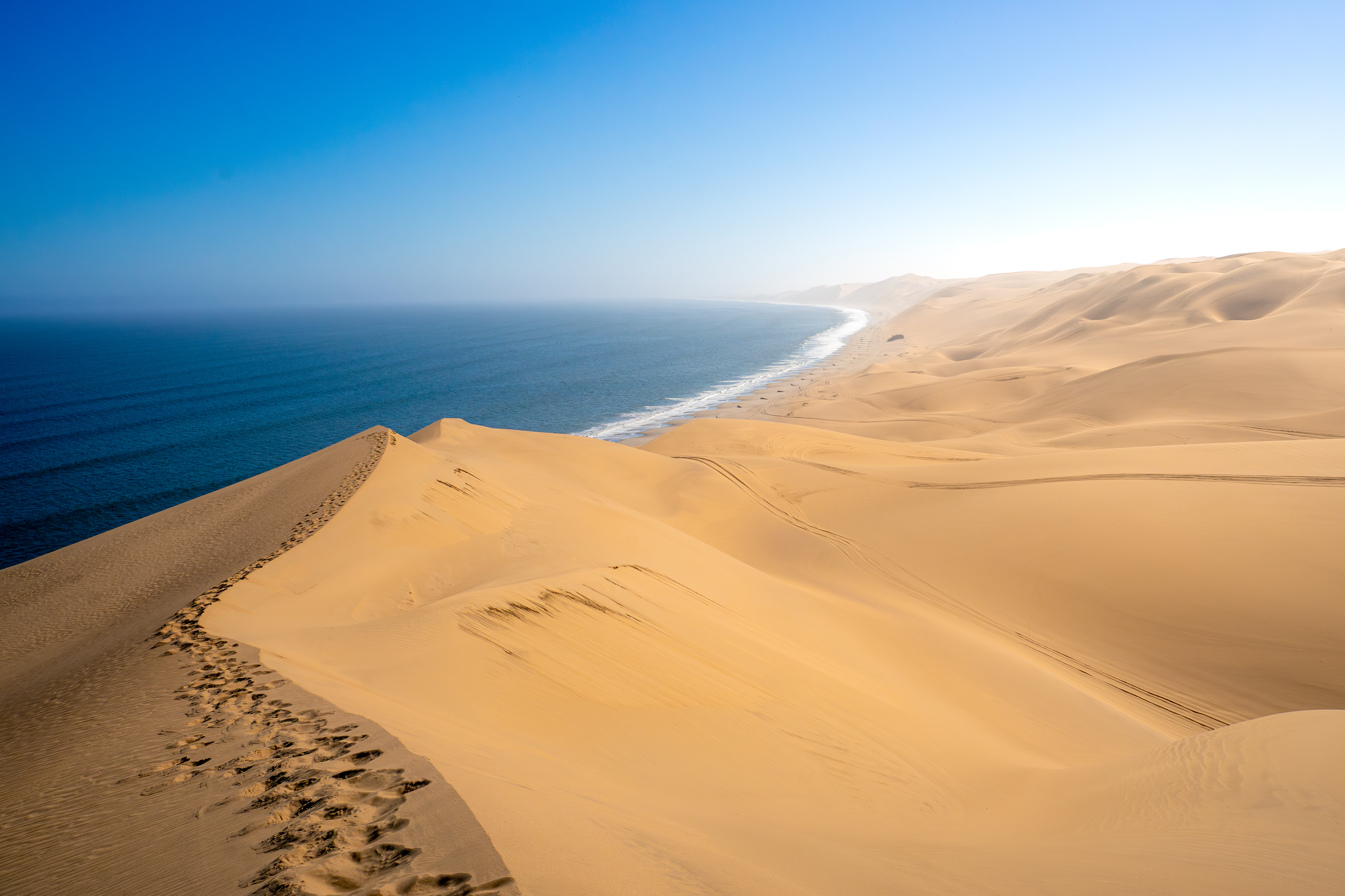 Golden sand dunes meet a flat cobalt-blue ocean under a clear sky at Walvis Bay, Namibia.