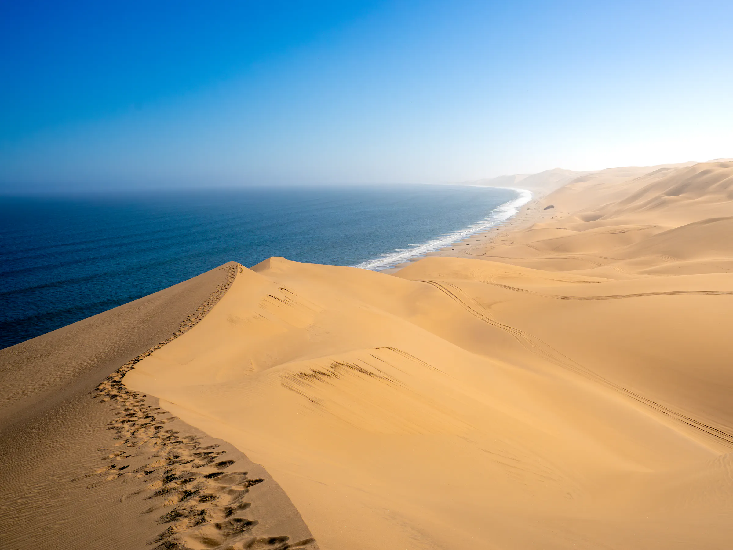 Golden sand dunes meet a flat cobalt-blue ocean under a clear sky at Walvis Bay, Namibia.