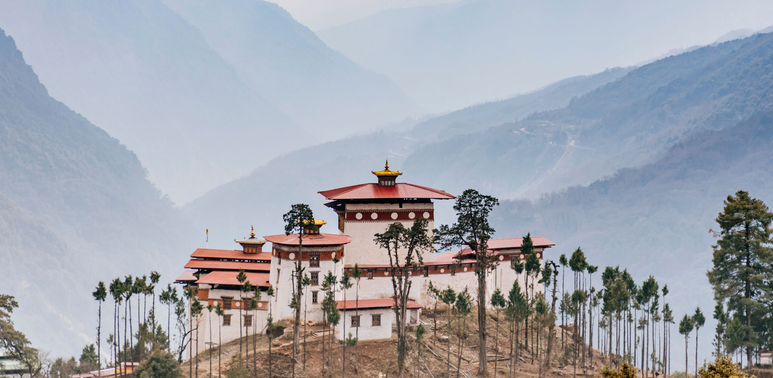 The Gasa Dzong fortress with white walls and a red tiered roof sits high in a green Bhutanese valley.