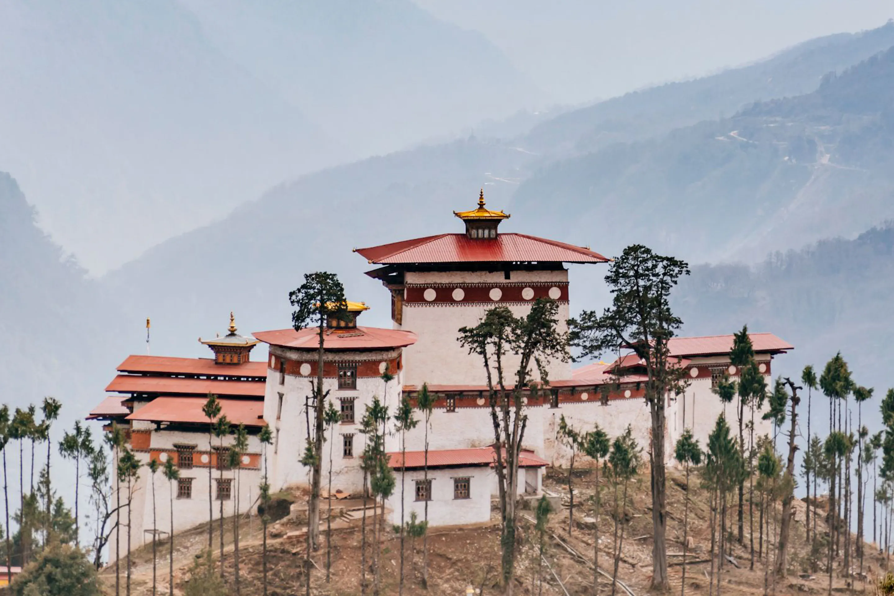 The Gasa Dzong fortress with white walls and a red tiered roof sits high in a green Bhutanese valley.