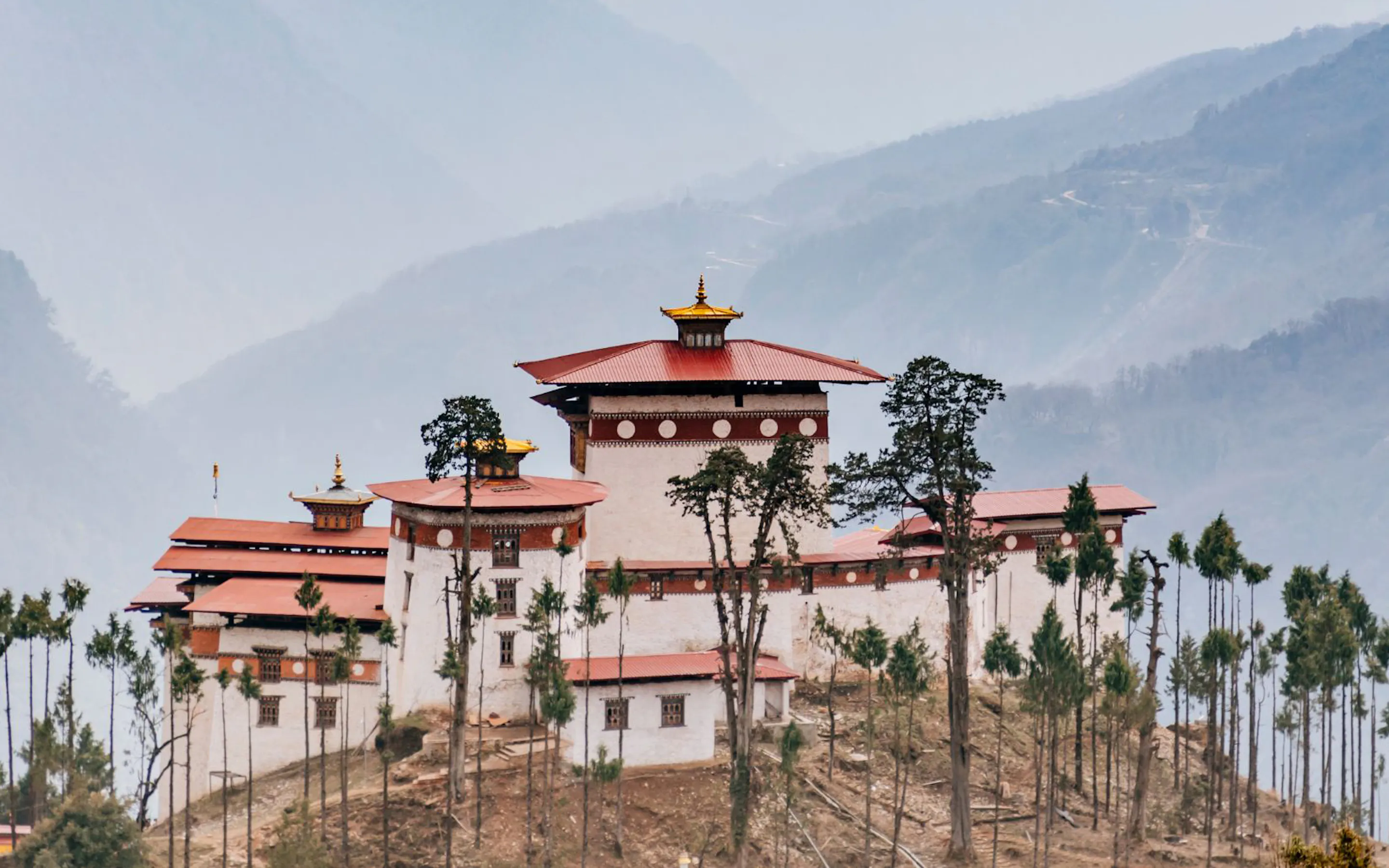 The Gasa Dzong fortress with white walls and a red tiered roof sits high in a green Bhutanese valley.