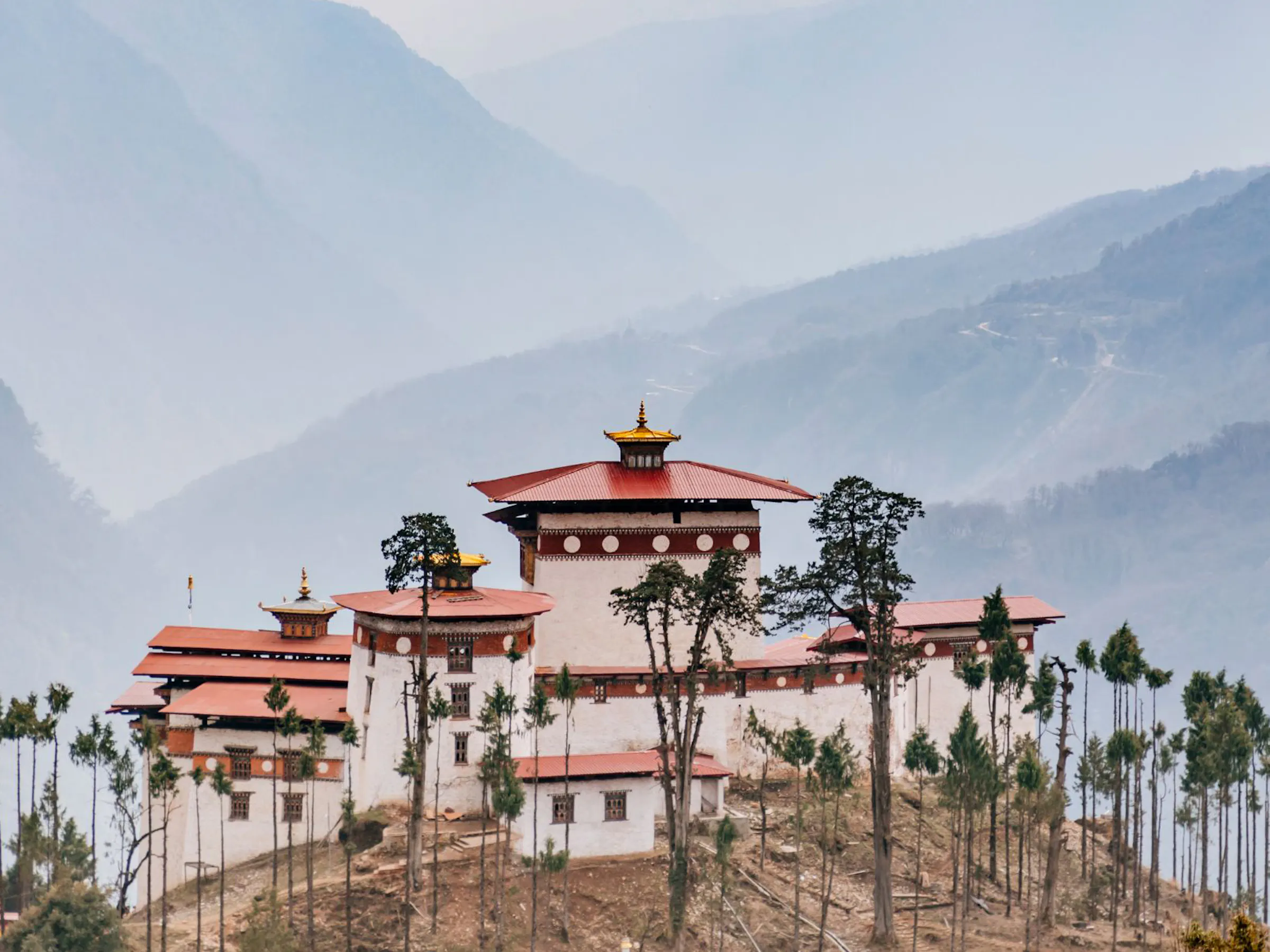 The Gasa Dzong fortress with white walls and a red tiered roof sits high in a green Bhutanese valley.