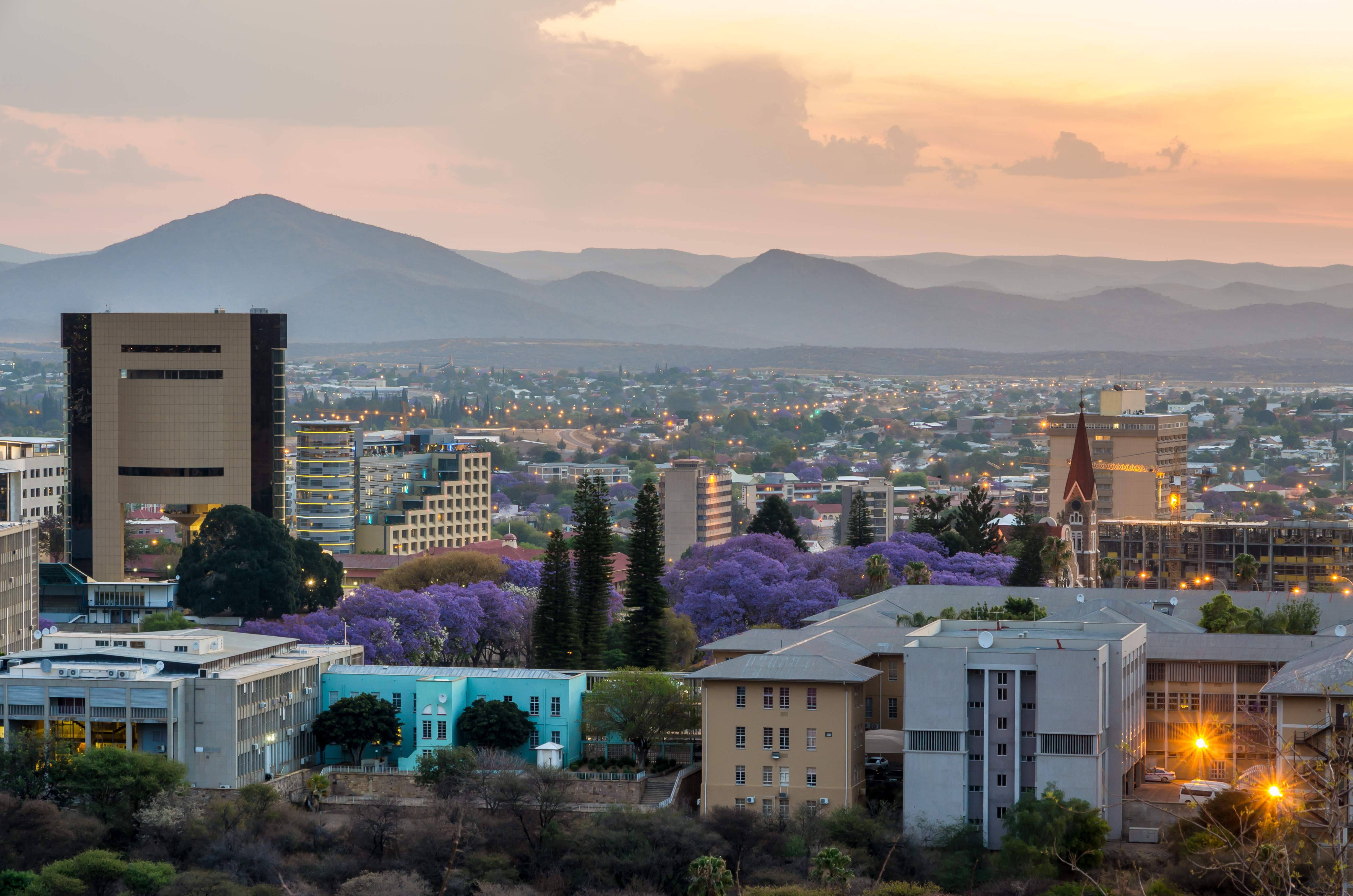 Windhoek's low-rise skyline and a red-roofed church spread across a wide valley under blue sky.
