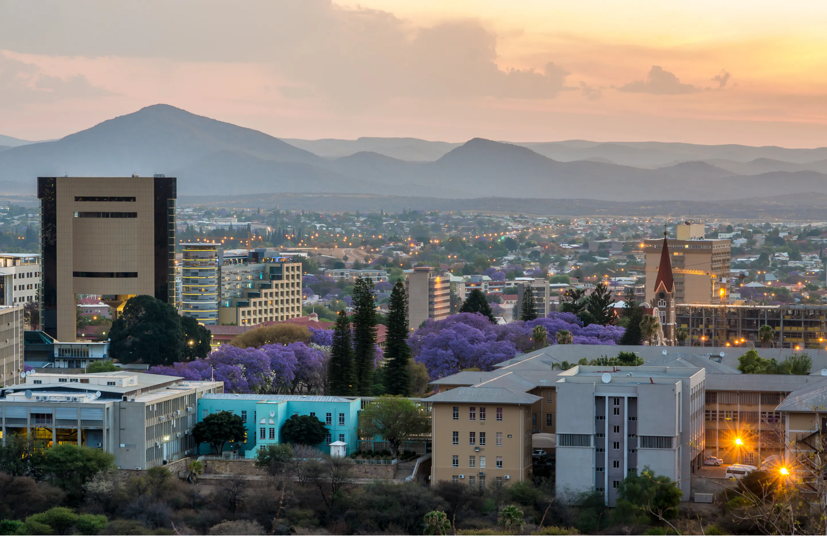 Windhoek's low-rise skyline and a red-roofed church spread across a wide valley under blue sky.